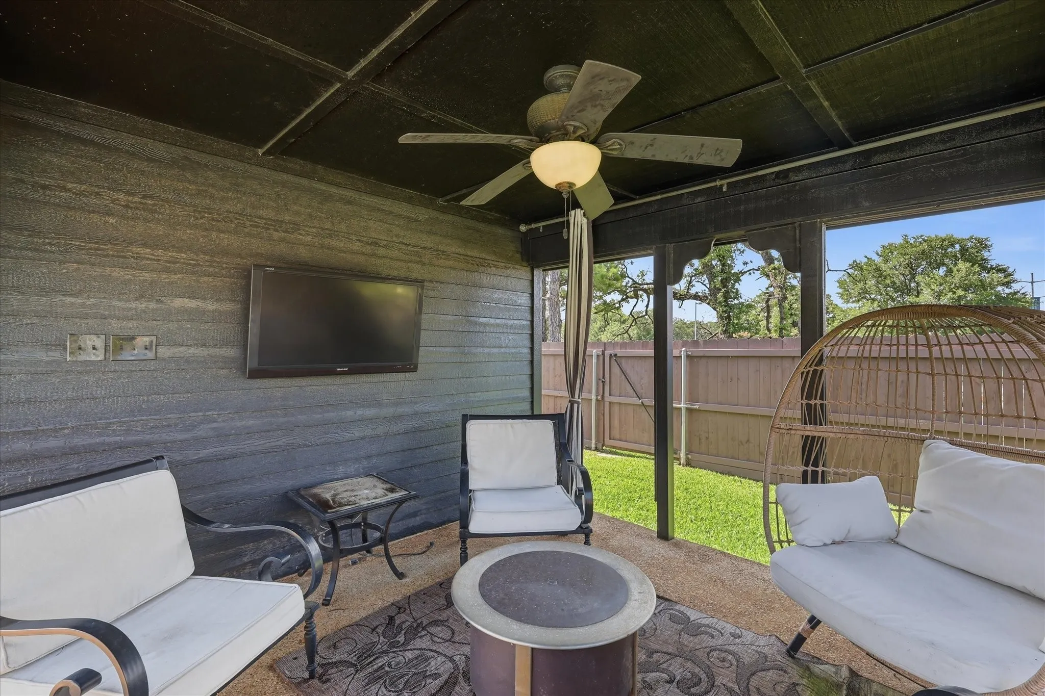 Patio cabana featuring a ceiling fan with integrated lighting, textured wall paneling, and a mounted television