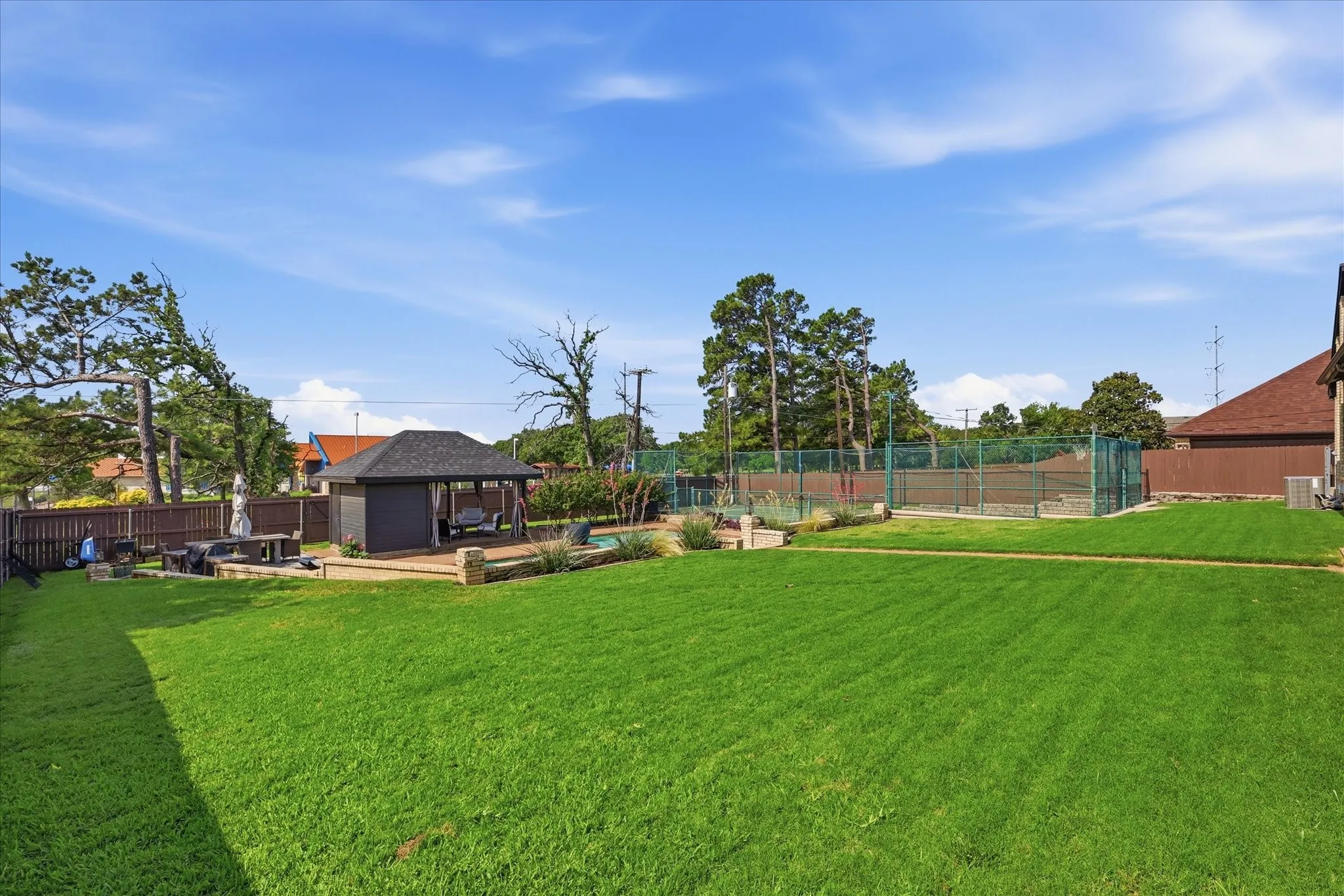 Expansive green lawn with a dedicated tennis court, a built-in gazebo, and a fenced perimeter