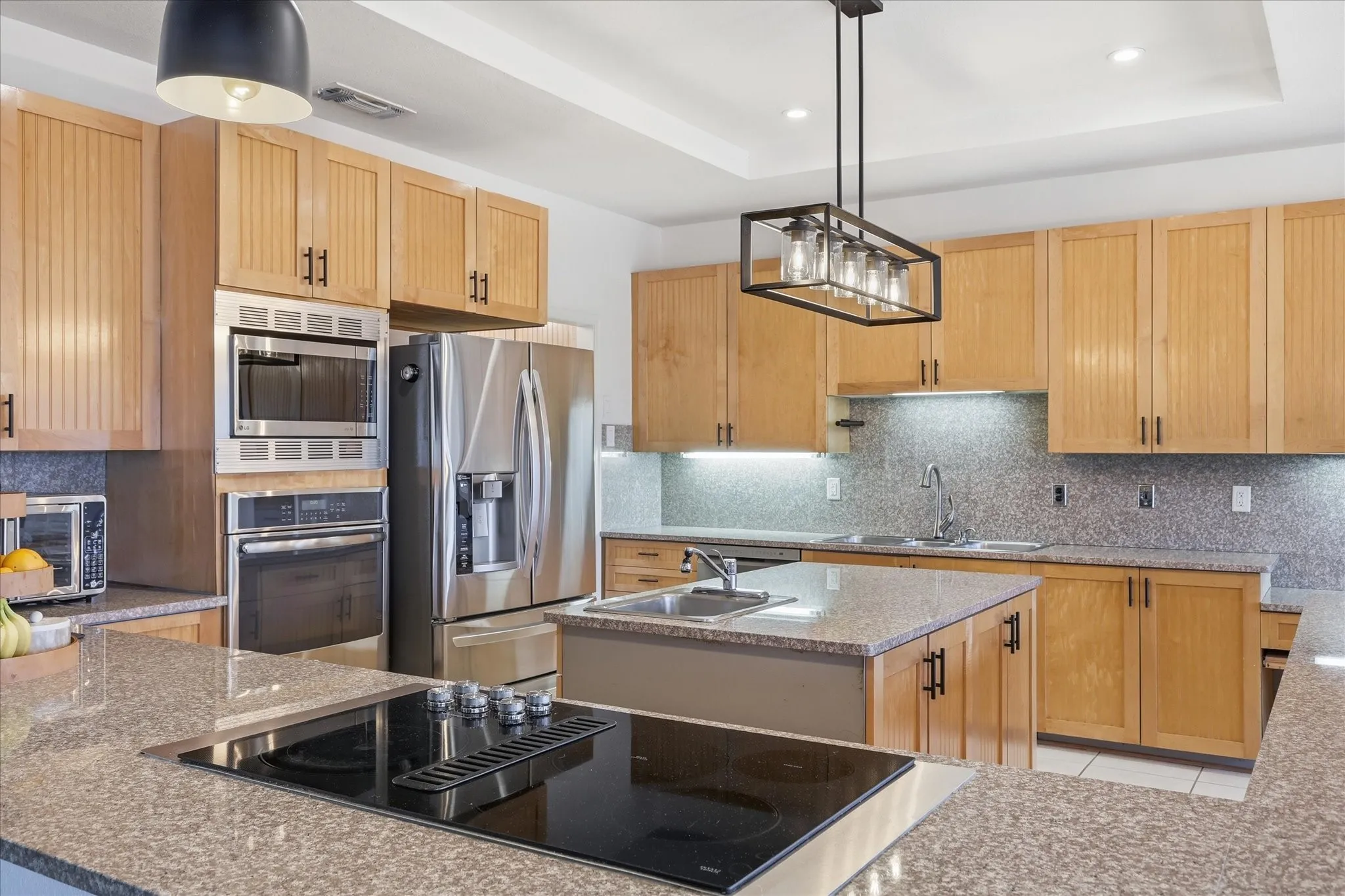 Large kitchen with two sinks, ample storage and counter space, electric cooktop with down-draft vent, under-cabinet lighting and modern light fixtures.