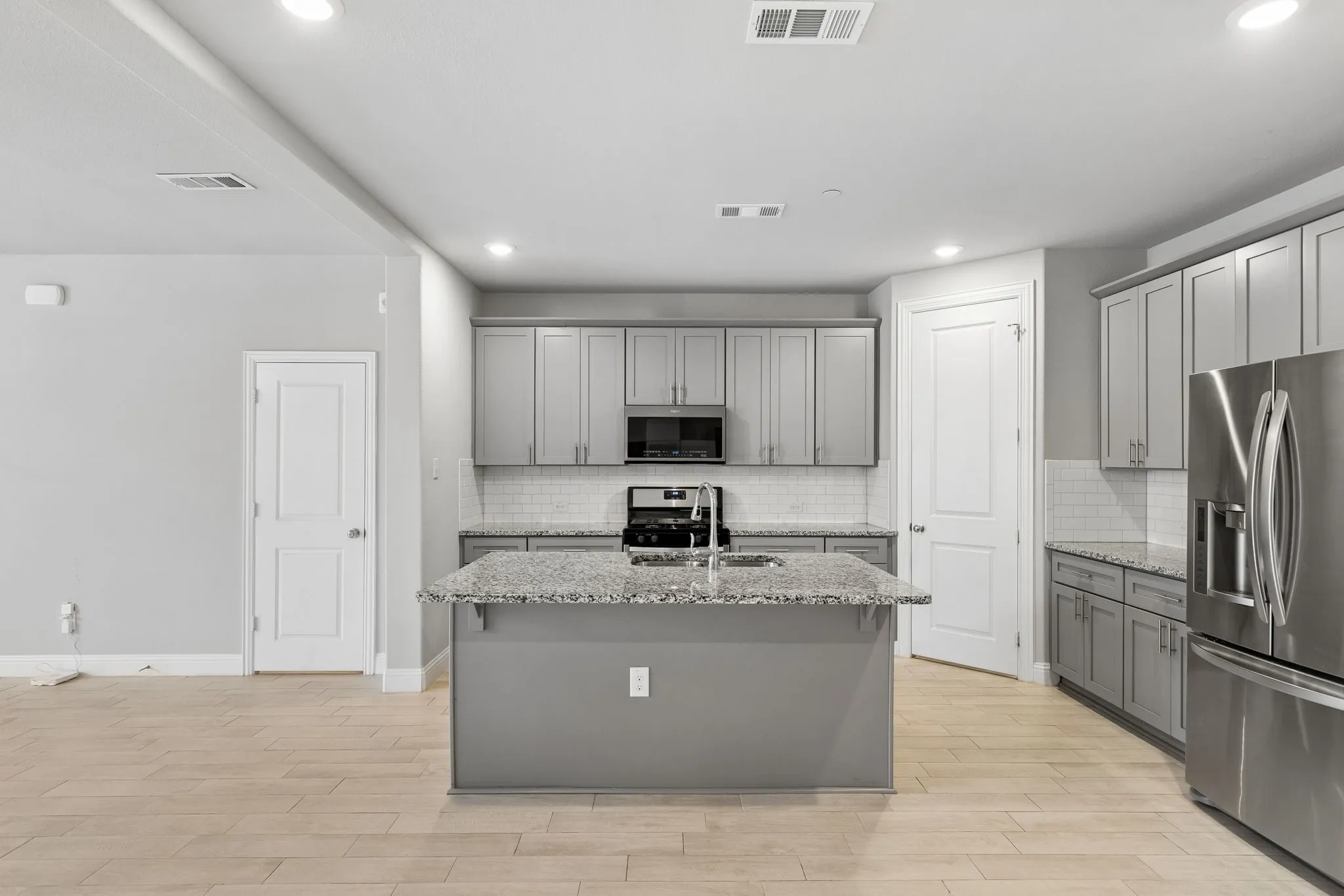 Contemporary kitchen featuring light wood-finish flooring, recessed lighting, gray cabinetry, and a granite island with an integrated sink