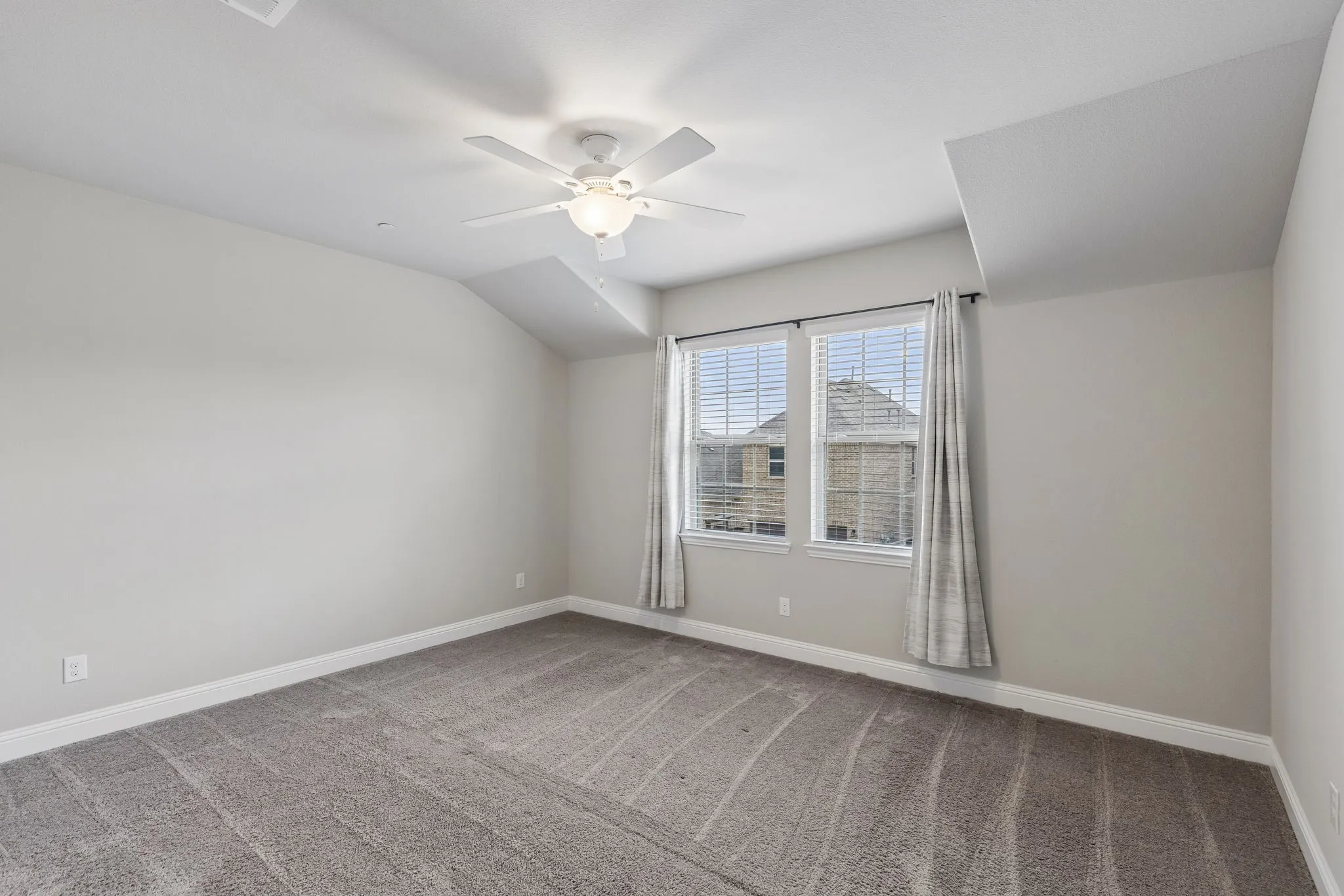 Carpeted room featuring a ceiling fan with integrated lighting, two windows with blinds.