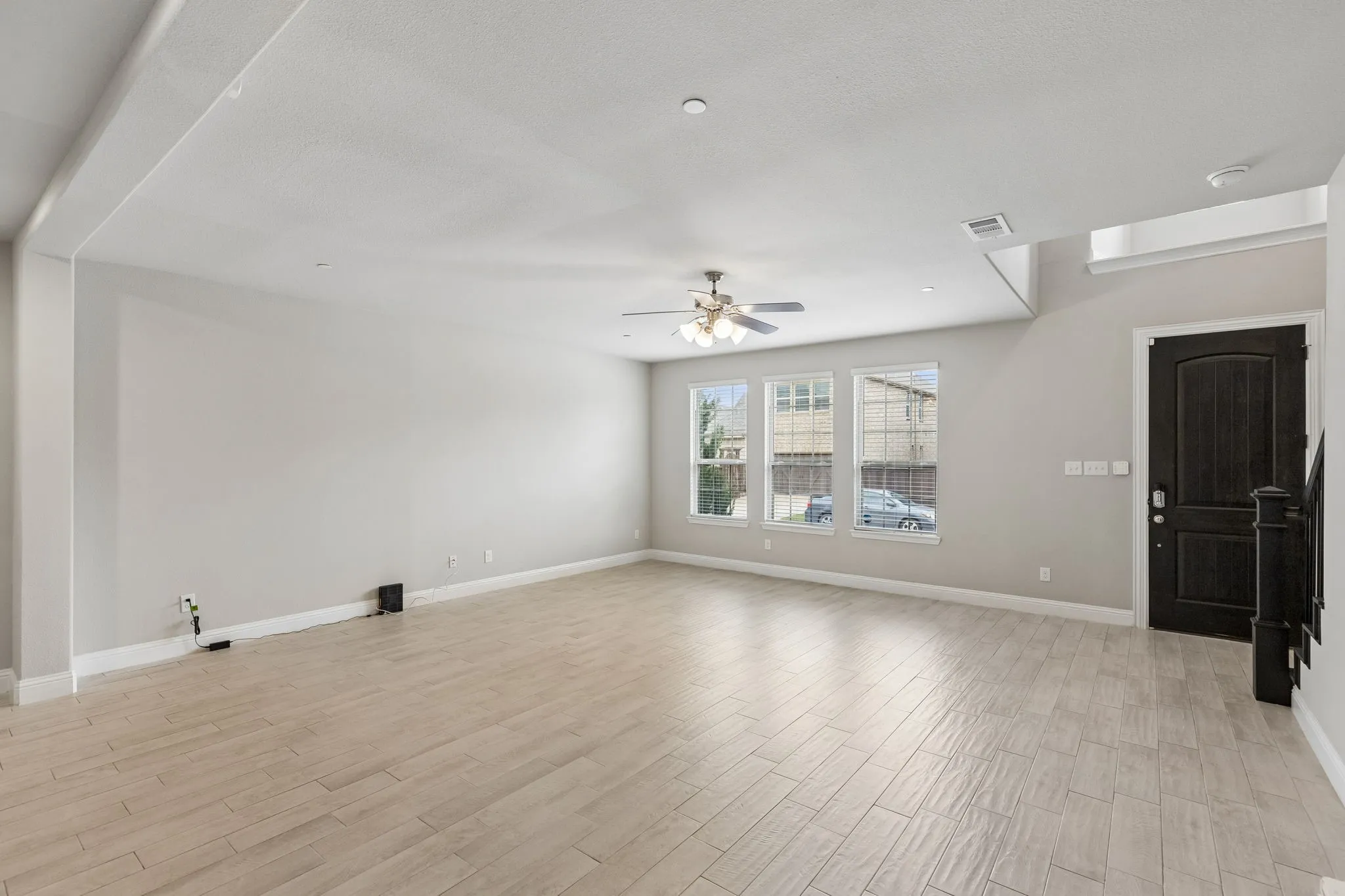 Spacious living area featuring light wood-finish flooring, a contemporary ceiling fan, and multiple windows providing natural illumination