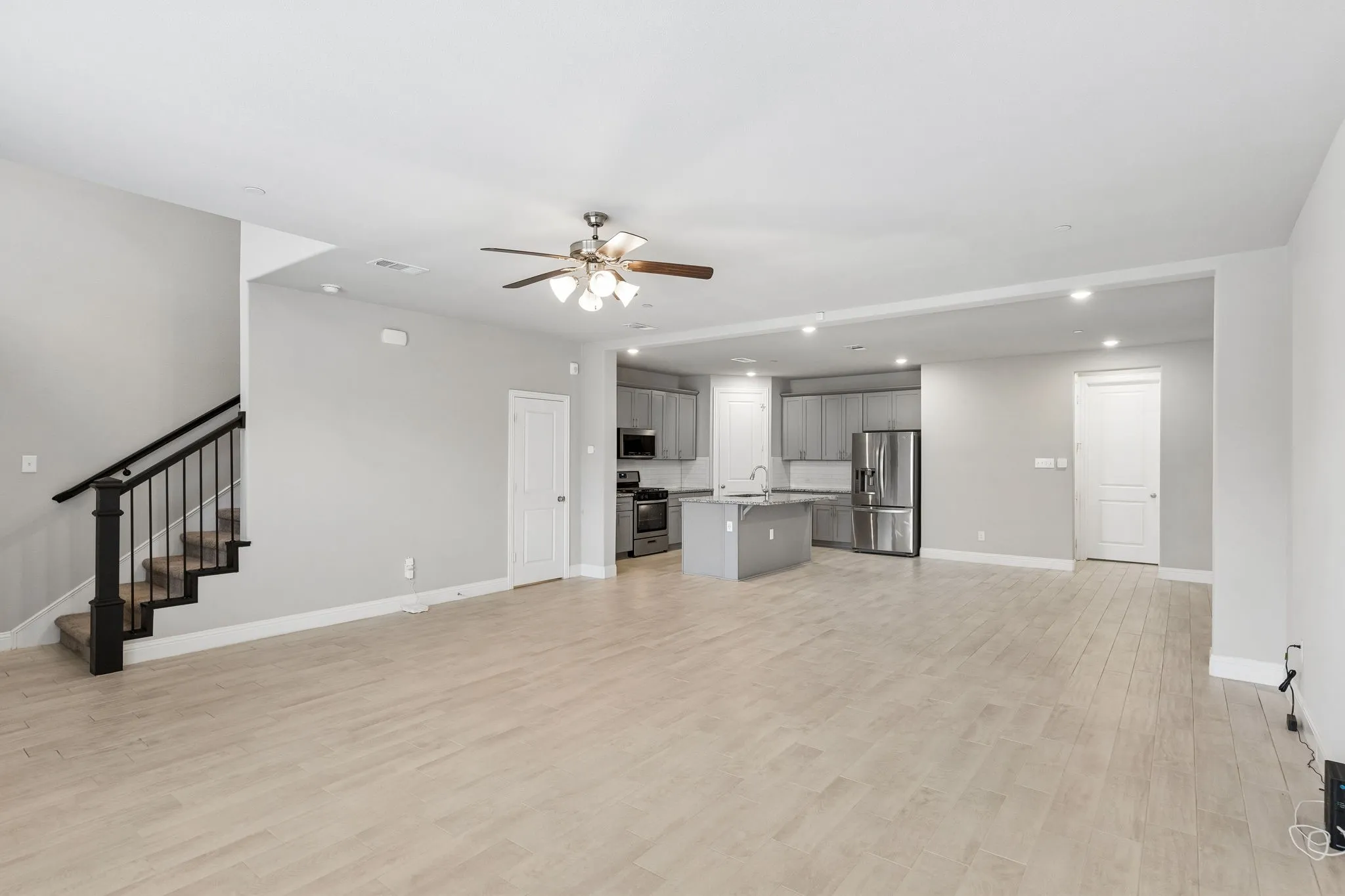 Open-concept living area featuring light wood-finish flooring, a contemporary staircase with dark wood newel posts and metal balusters, and recessed lighting