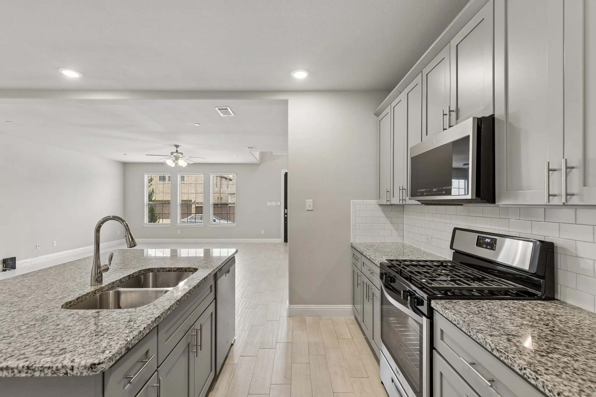 Kitchen featuring granite countertops, stainless steel appliances, grey cabinetry with brushed nickel hardware, and subway tile backsplash
