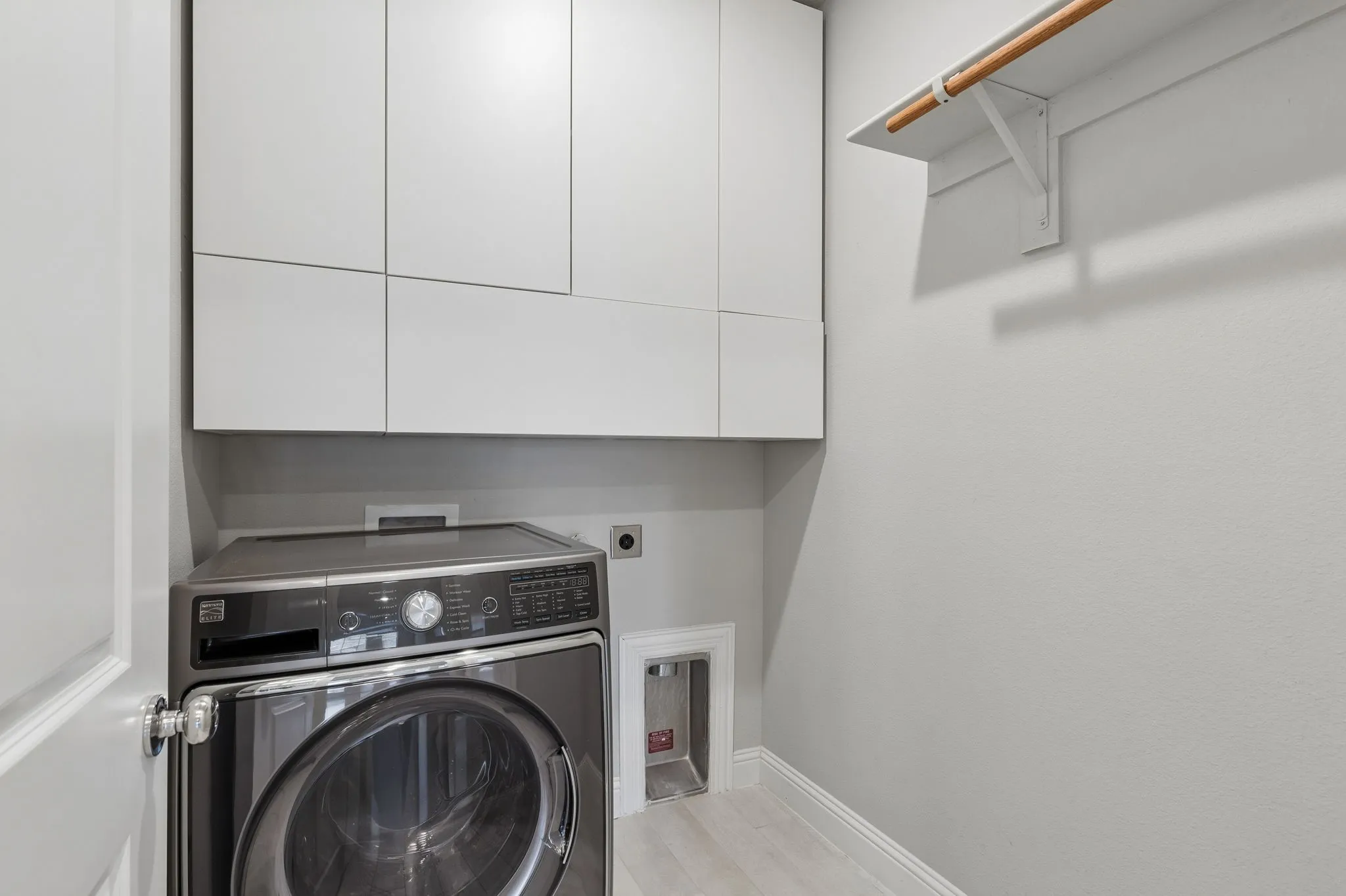 Dedicated laundry area featuring light wood-finish flooring, and built-in storage