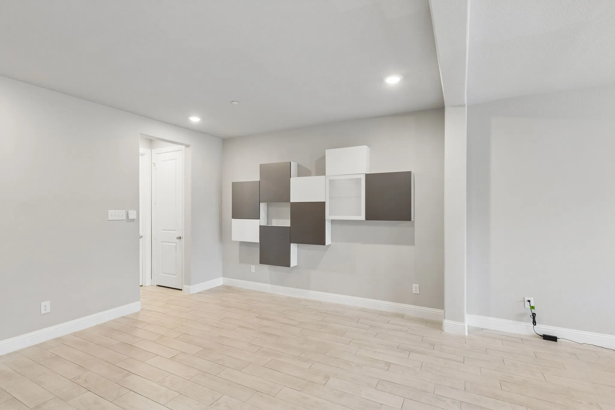 Spacious room featuring light-toned wood-finish flooring, recessed lighting, and a modern wall-mounted shelving unit