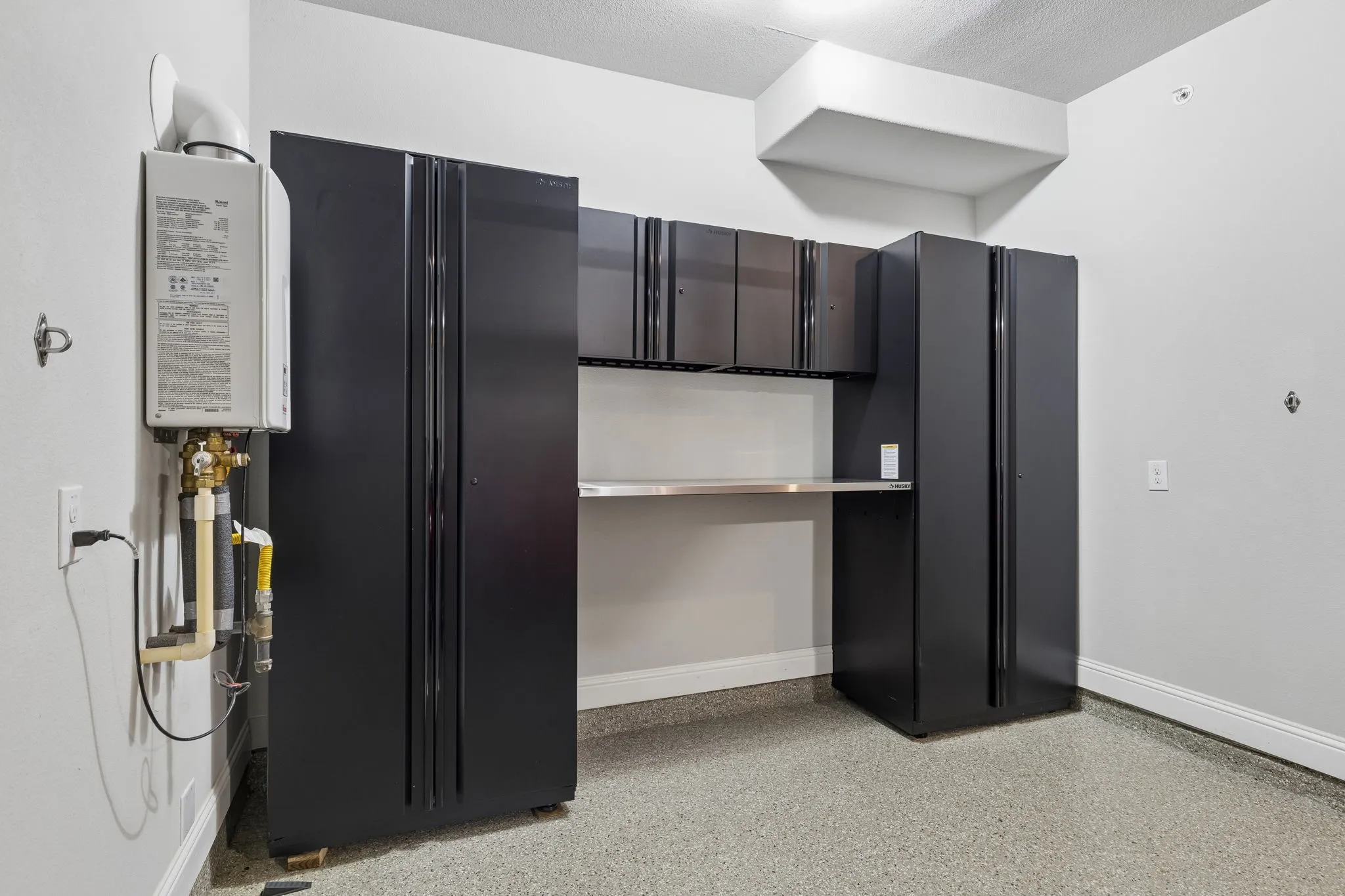 Garage featuring extensive Husky built-in cabinetry, durable epoxy flooring, and a tankless water heater