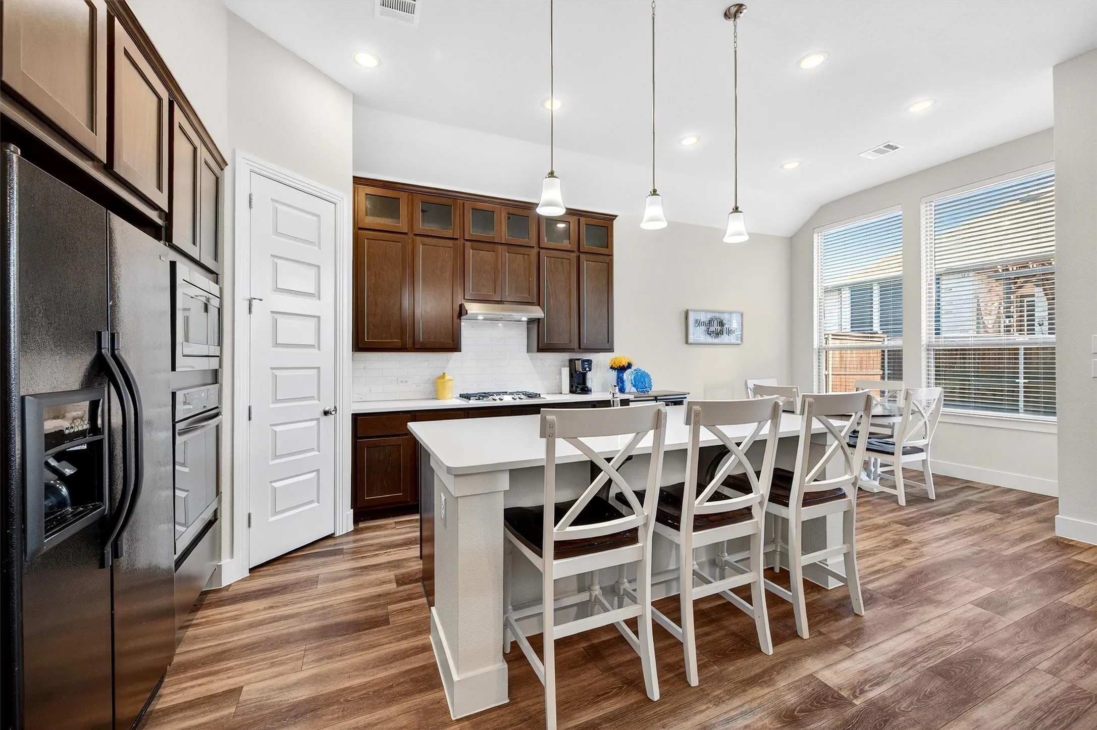 Kitchen with stainless steel appliances, backsplash, glass insert cabinets, dark wood finished floors, and a kitchen bar