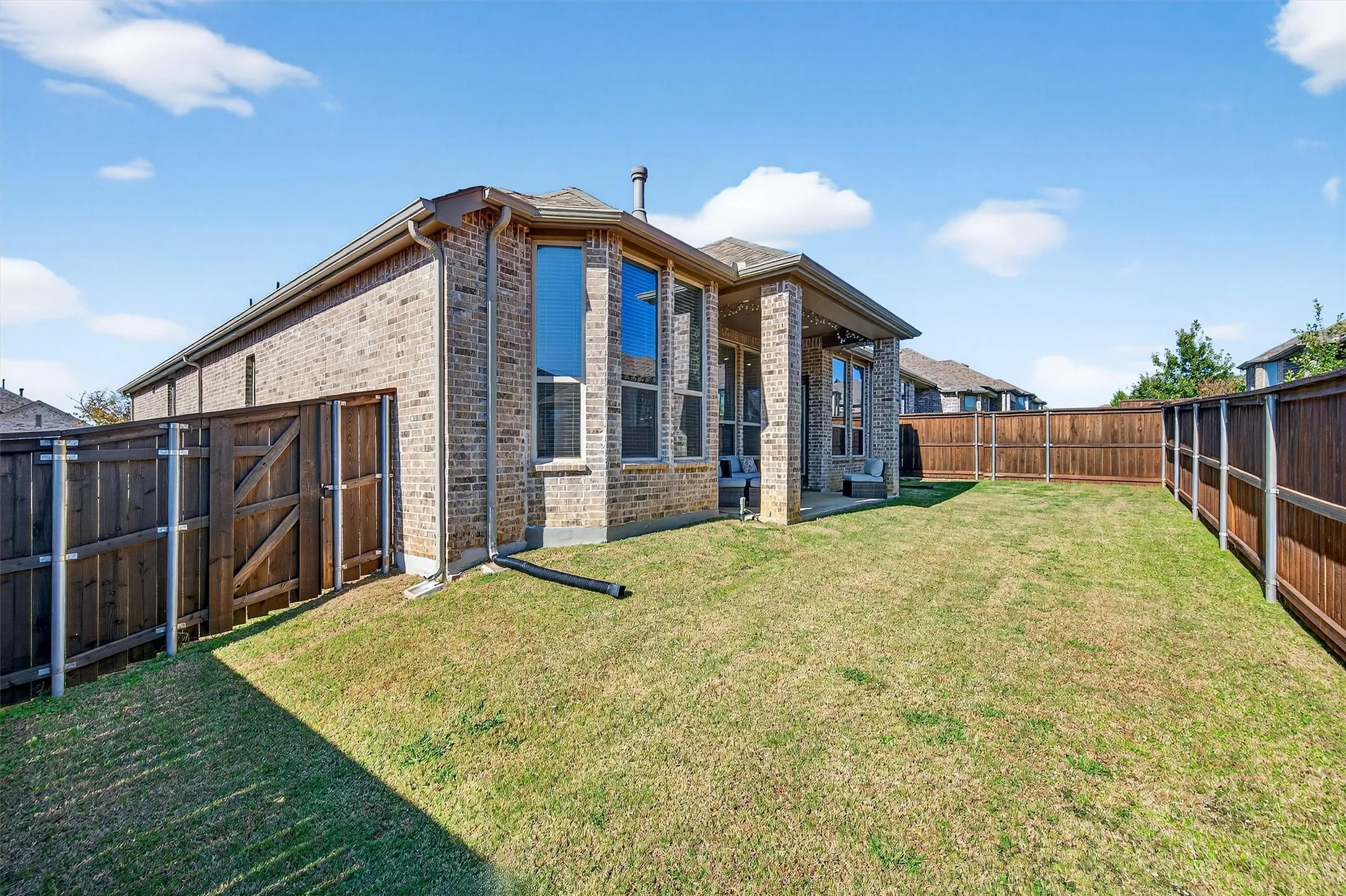Back of house with brick siding, a patio, a fenced backyard, and a gate