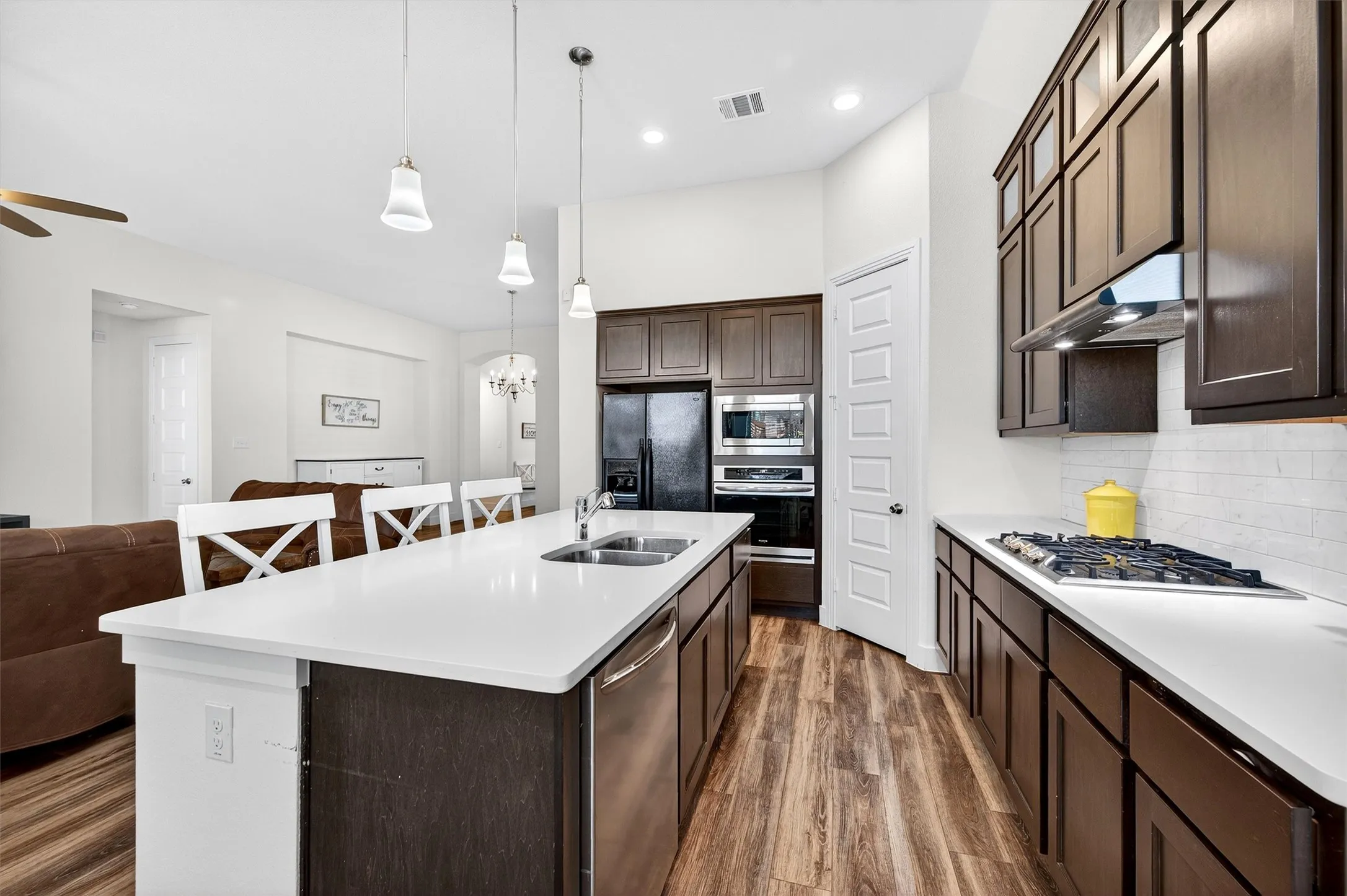 Kitchen featuring dark brown cabinets, dark wood-type flooring, open floor plan, stainless steel appliances, and a center island with sink