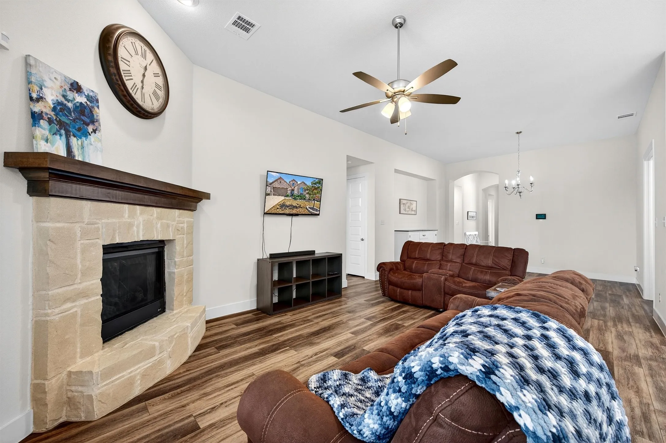 Living room featuring wood finished floors, a chandelier, ceiling fan, a fireplace, and arched walkways