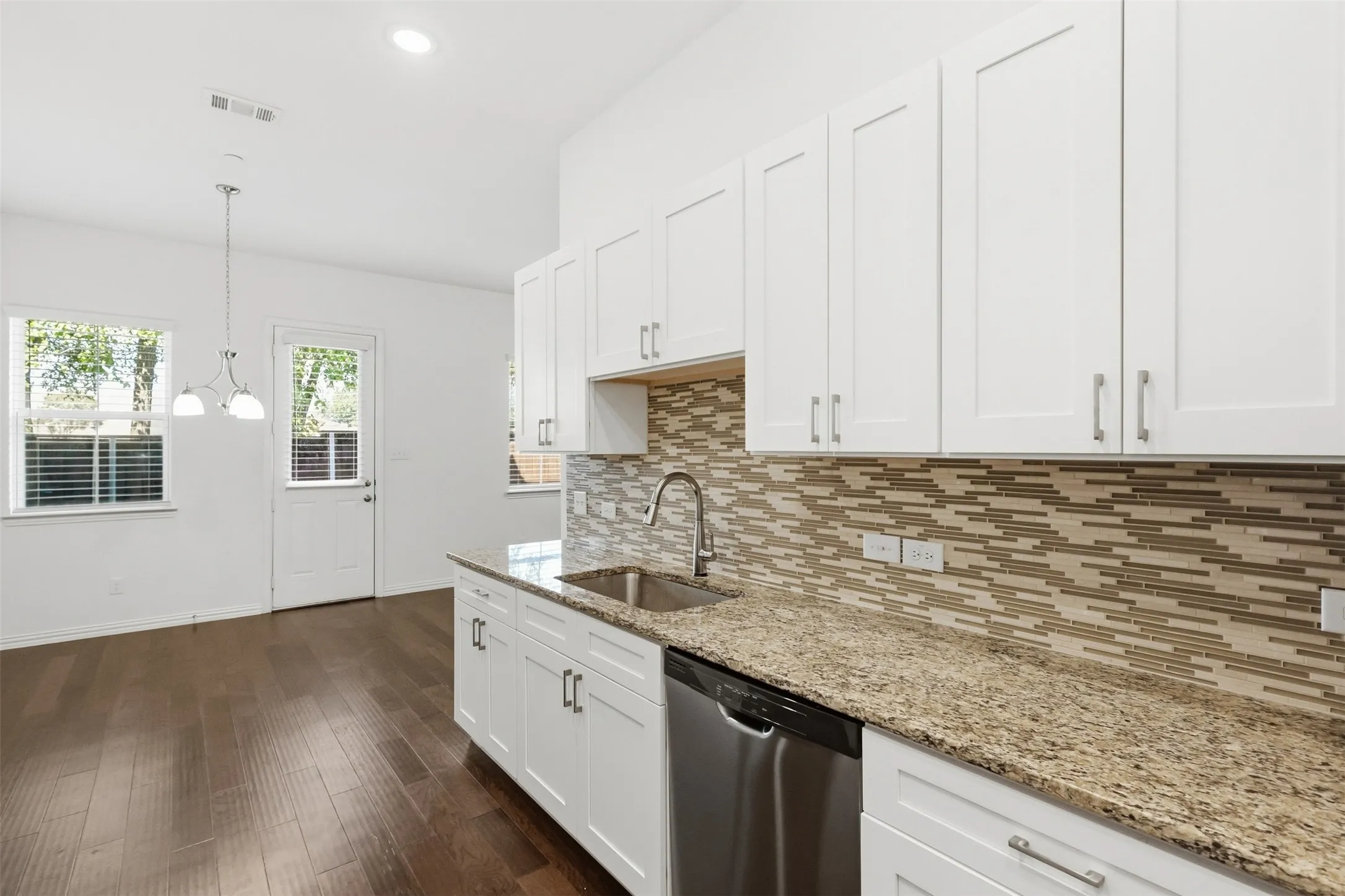 White shaker-style cabinetry, stainless steel dishwasher, speckled countertop, mosaic tile backsplash, and dark wood flooring