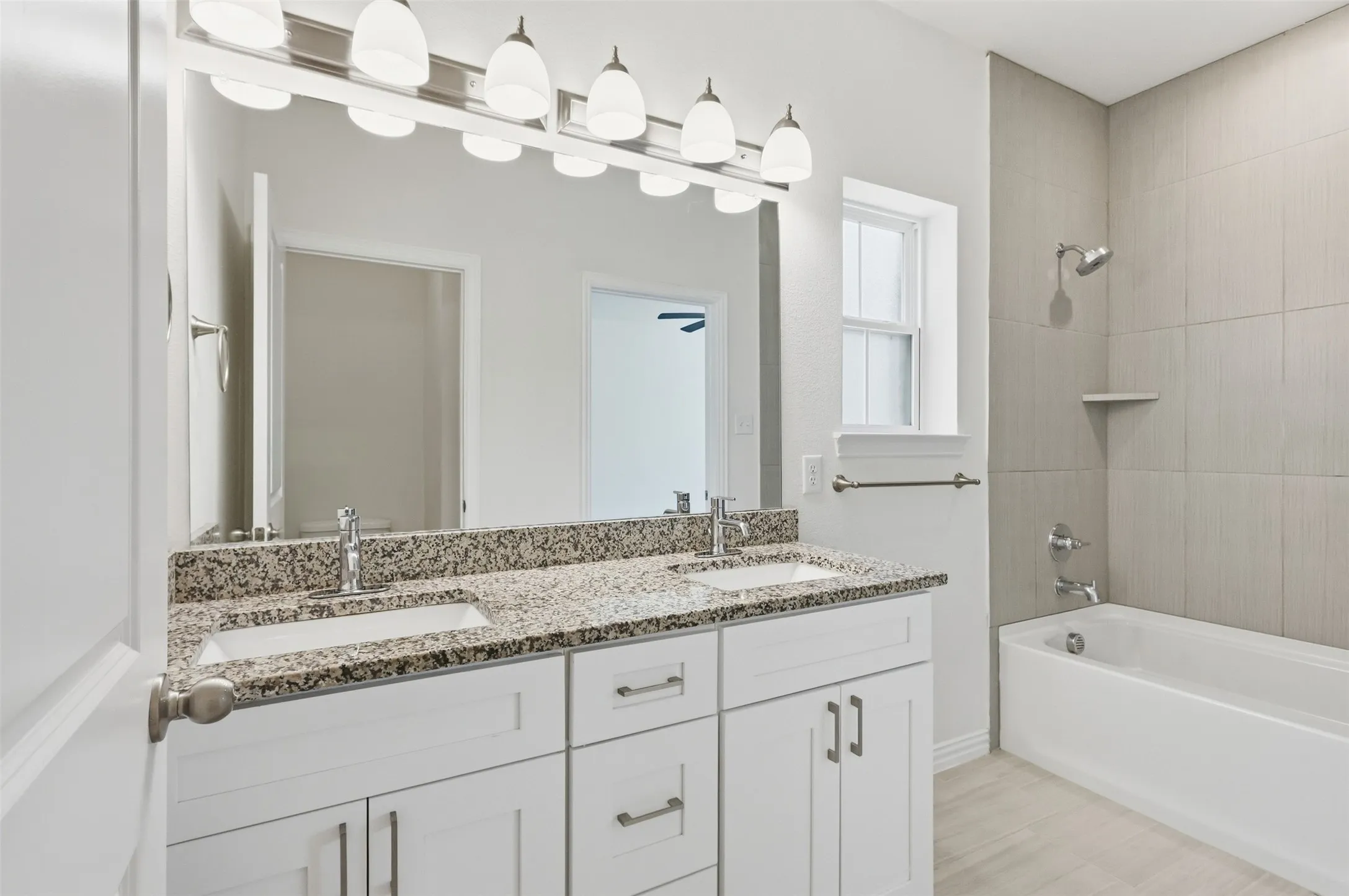 Primary ensuite bathroom with dual vanity with granite countertop and undermount sinks, white cabinetry with chrome hardware, and a framed mirror with a six-light fixture and water closet
