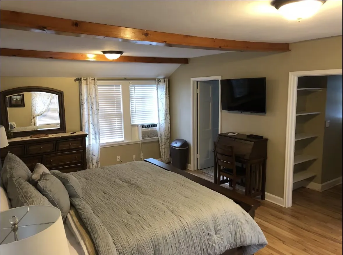 Upstairs bedroom featuring wood-finish flooring, exposed ceiling beams, and dual windows with blinds