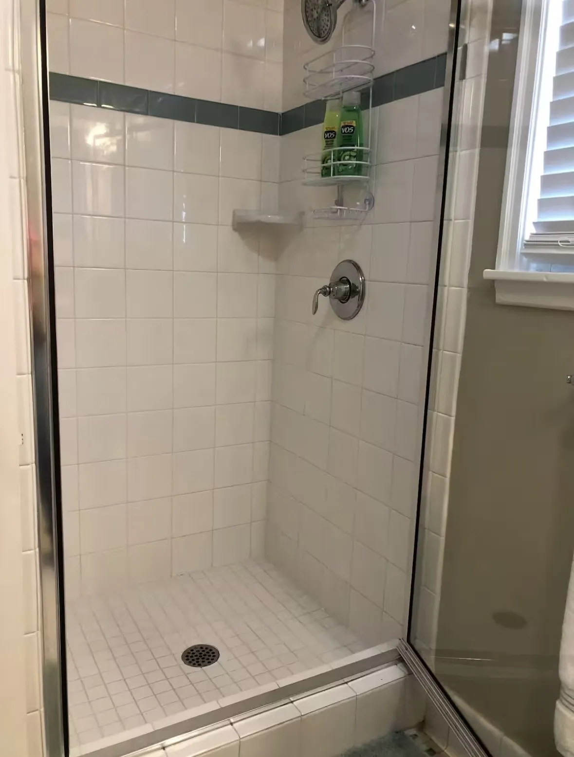 Upstairs tiled shower enclosure featuring white subway tile walls with a contrasting accent band, a white tiled floor, and a clear glass door