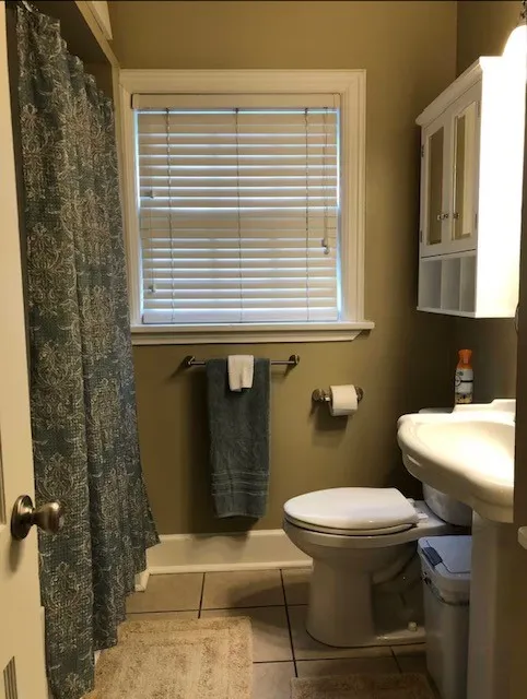 Bathroom featuring a window with blinds, a wall-mounted cabinet with glass doors, and tile flooring