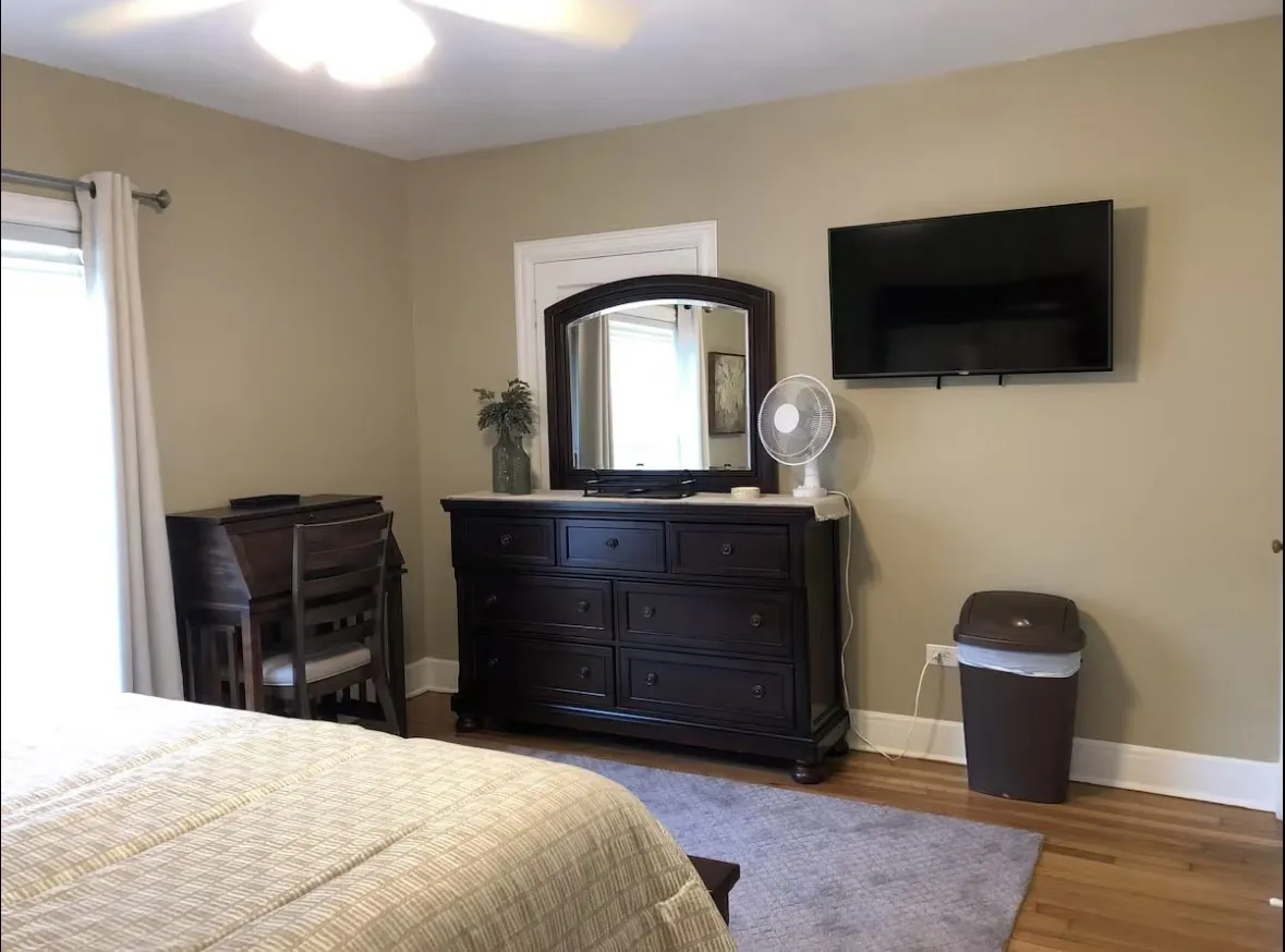 Upstairs bedroom with hardwood flooring with a soft area rug, neutral wall paint, and white trim