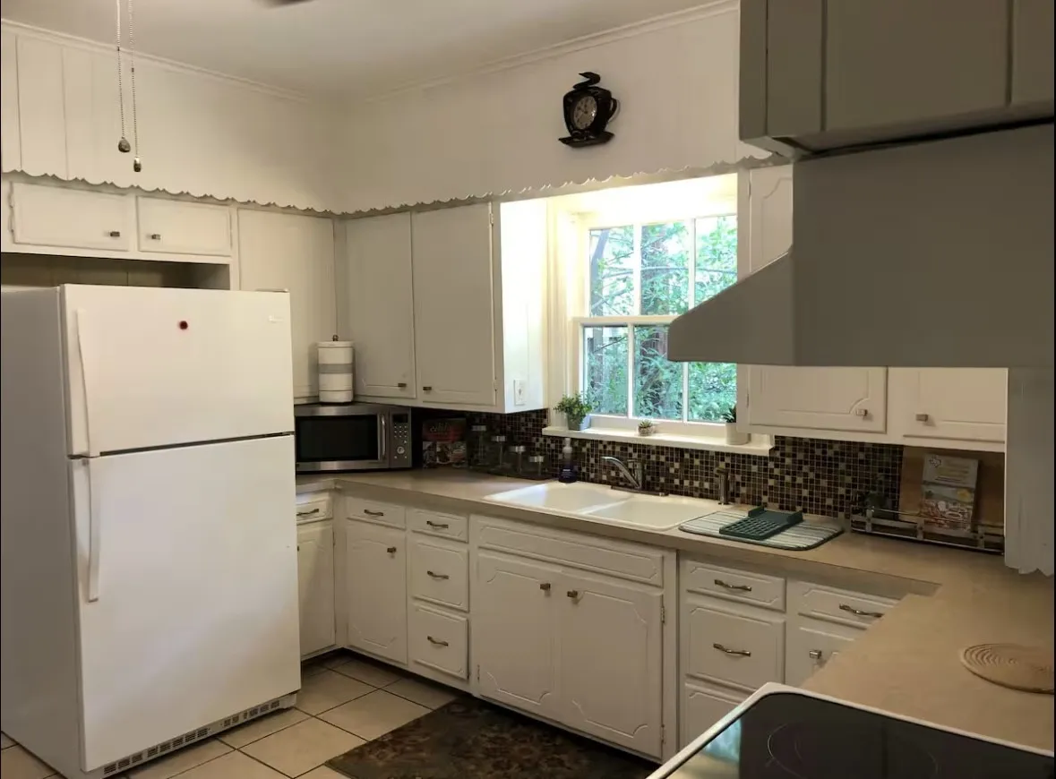Kitchen featuring white cabinetry with decorative scalloped trim, a dual basin sink, and a multi-toned mosaic tile backsplash