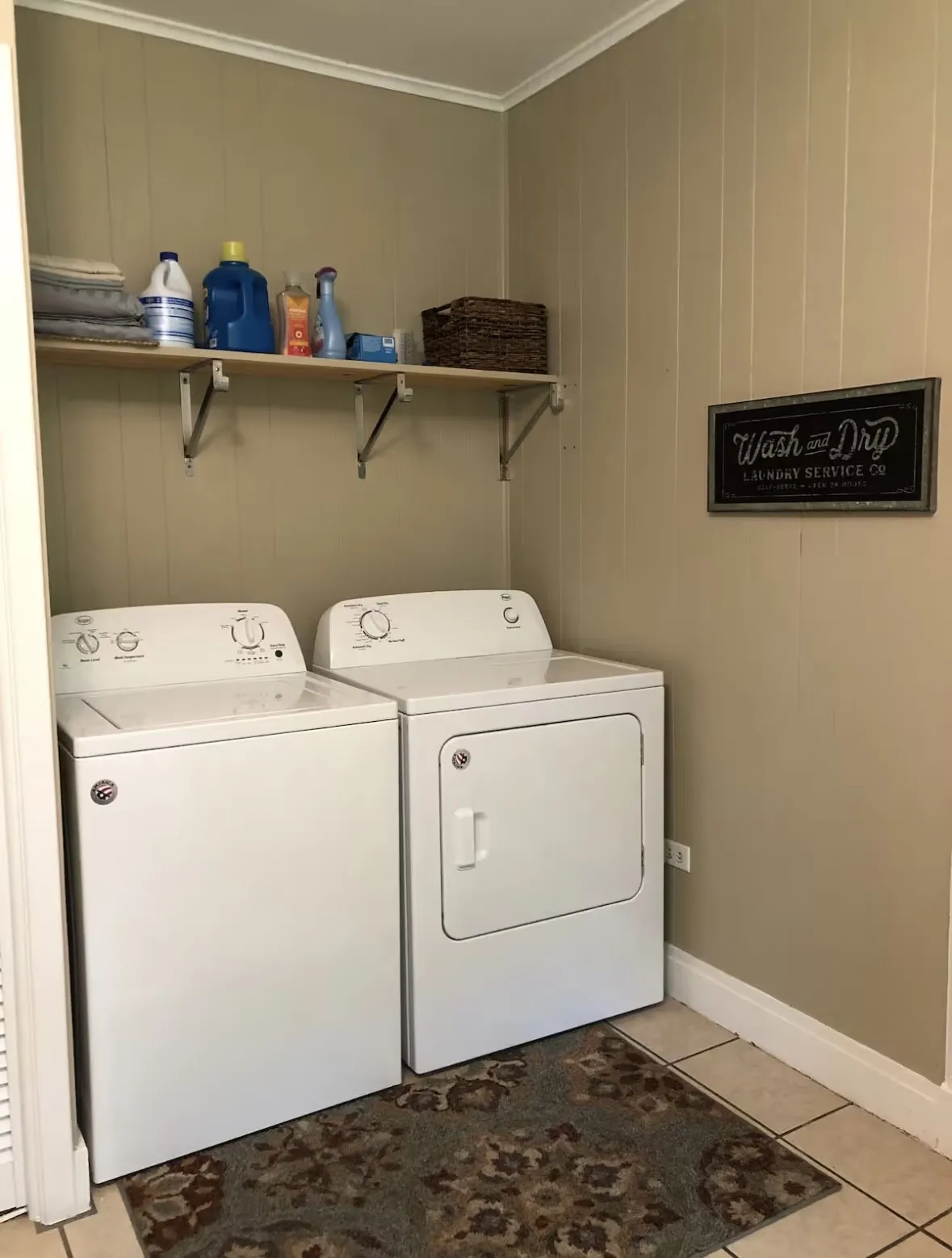 Dedicated laundry area featuring a washer and dryer, wood-finish shelving, vertical paneling, and tile flooring in Kitchen area