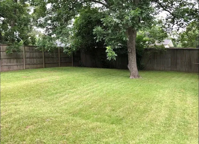 Expansive lawn area featuring  mature trees, perimeter wood fencing, and healthy grass.