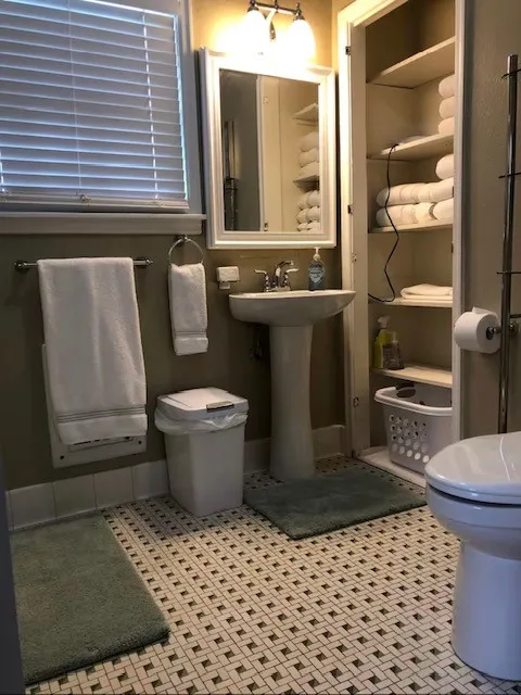 Upstairs Pedestal sink with chrome fixtures, wall-mounted mirror, and vanity lighting