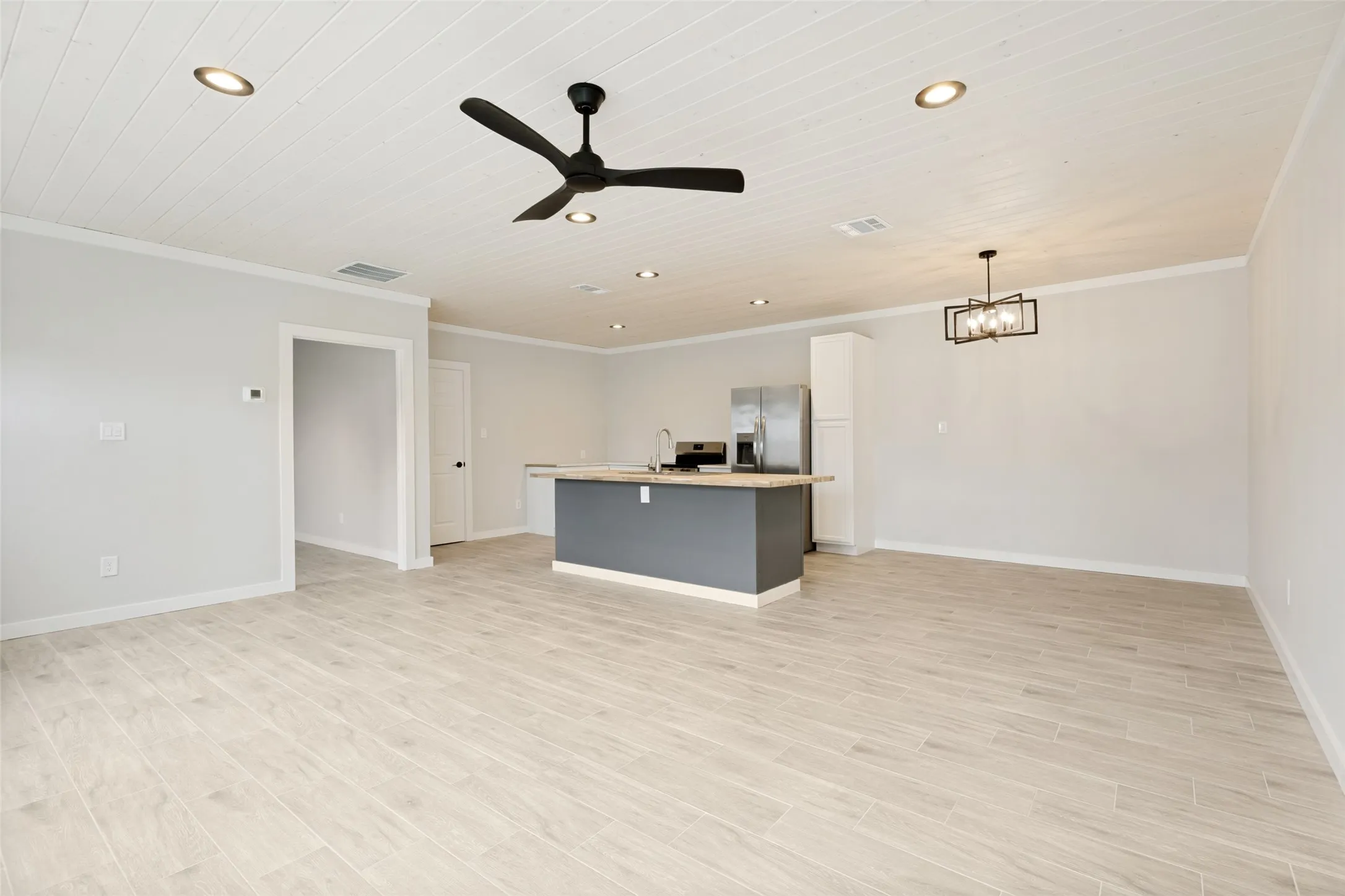 Guest house - Open-concept living area featuring light wood-finish flooring, a white shiplap ceiling, recessed lighting, a modern black ceiling fan, and a kitchen island with a light-colored countertop