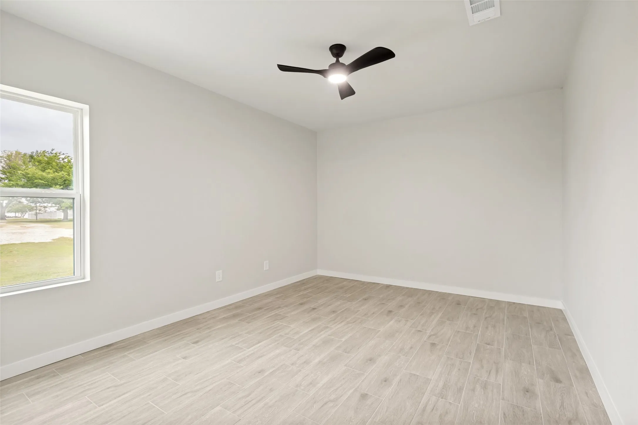 Guest house -Spacious room featuring light-toned walls, wood-look flooring, and a modern ceiling fan with integrated lighting