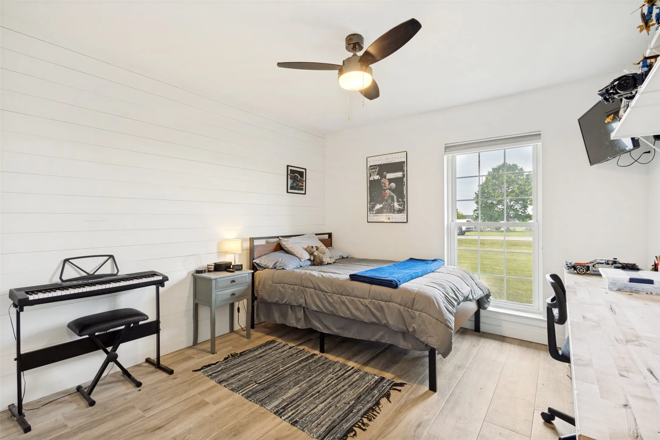 Bedroom featuring wood-finish flooring, a contemporary ceiling fan with integrated lighting, and a window with exterior views