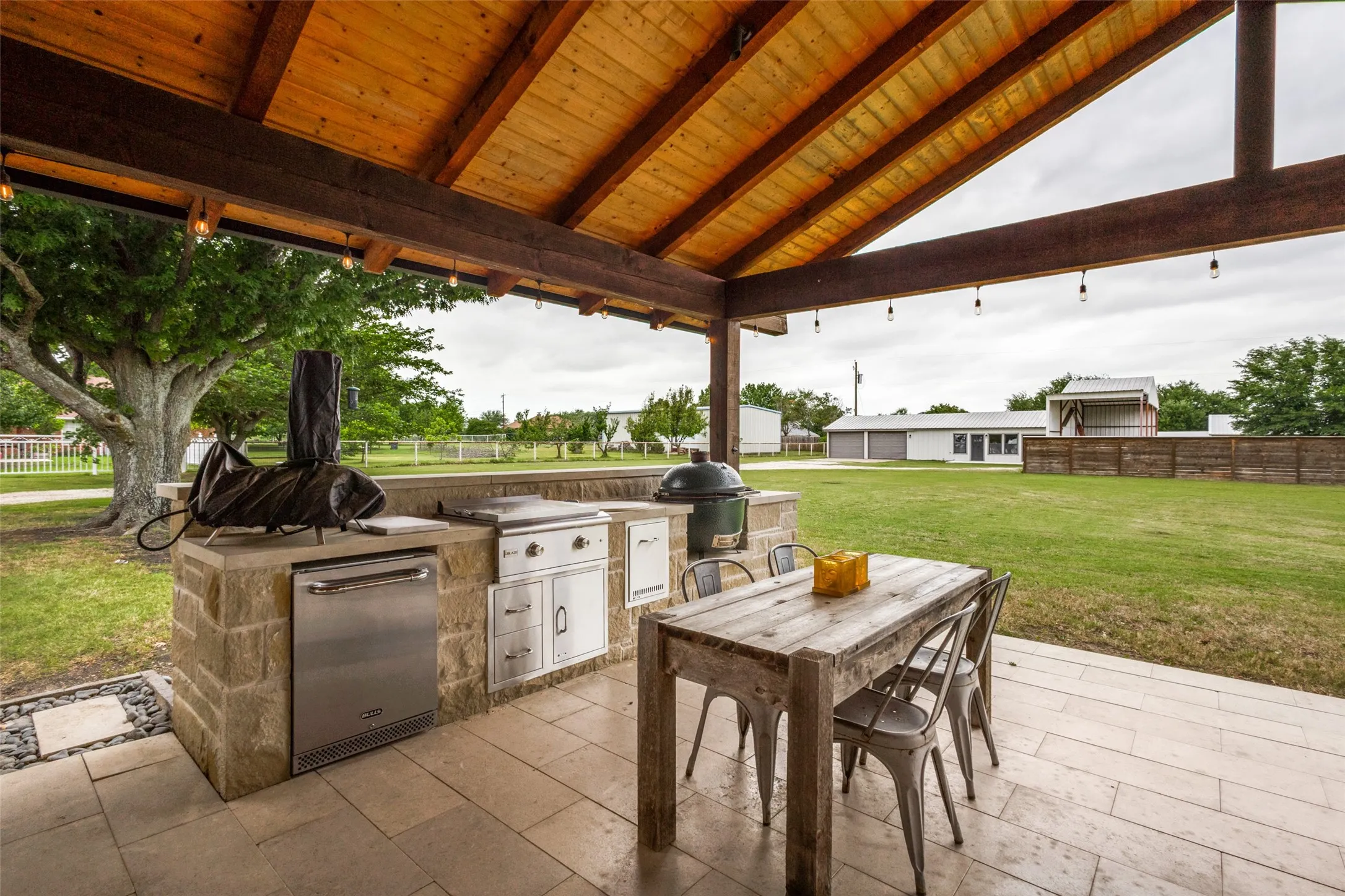 Expansive covered patio featuring a wood-plank ceiling with exposed beams, string lighting, and tile flooring