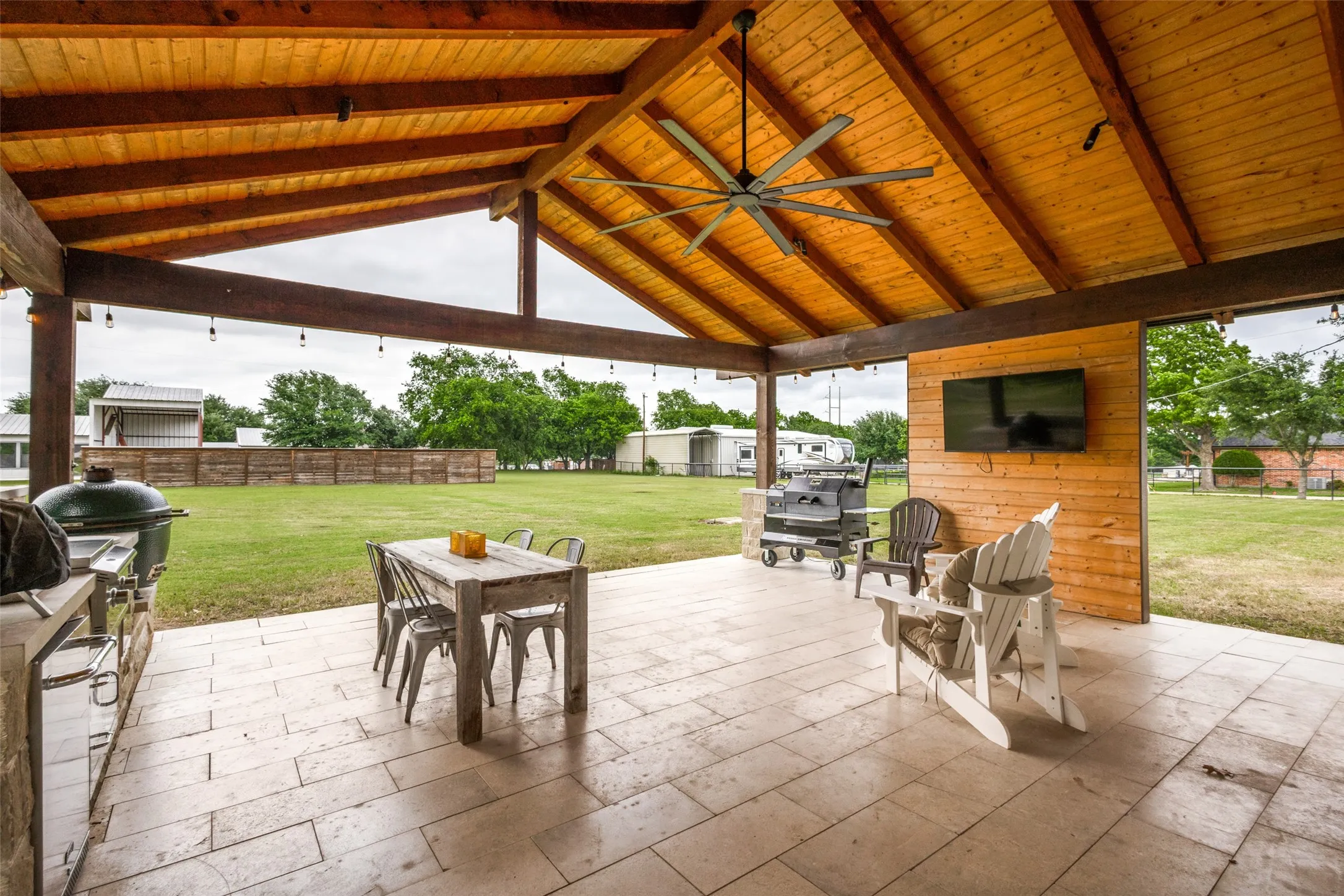 Expansive covered patio featuring a vaulted wood-paneled ceiling, exposed wood beams, and a large ceiling fan