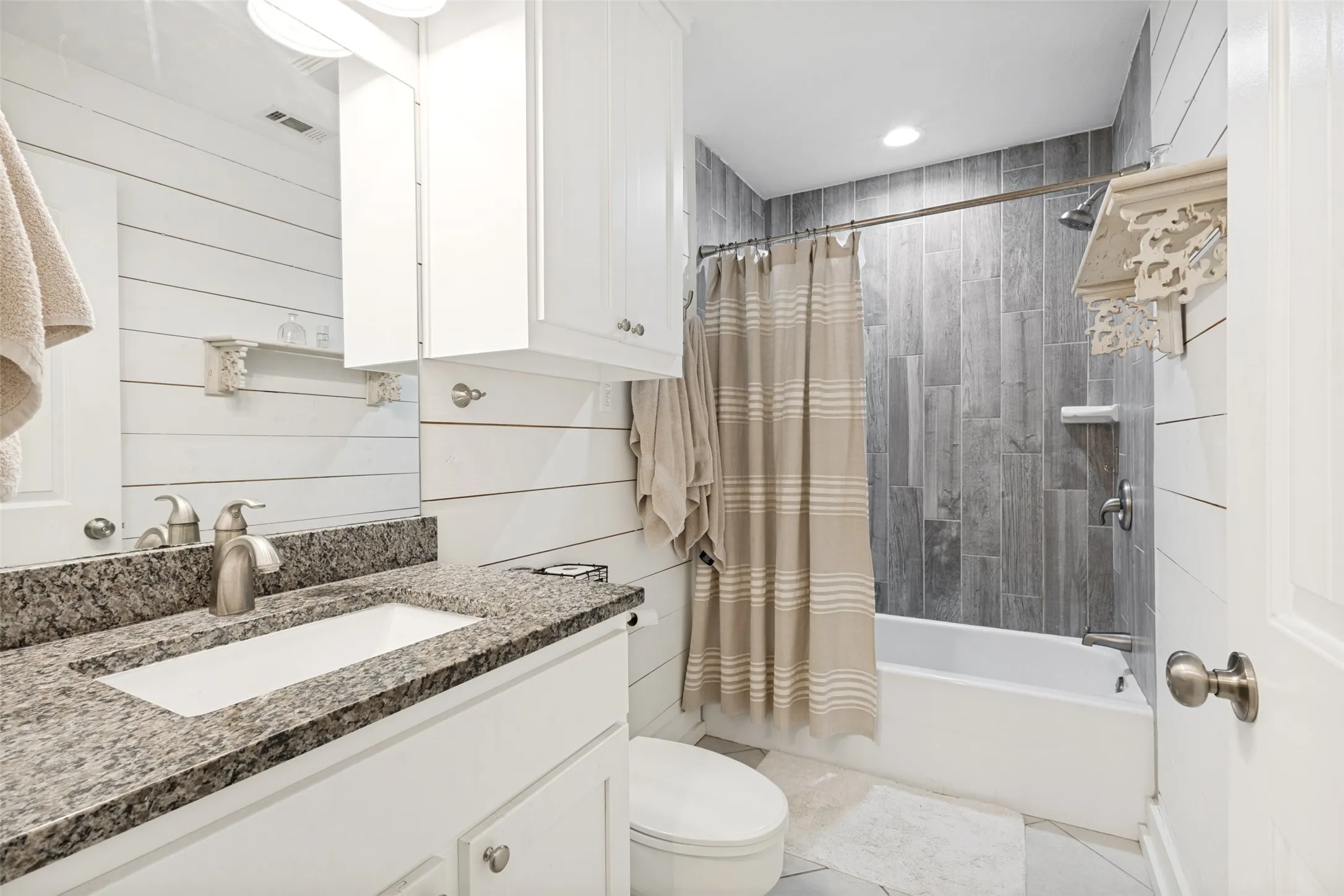 Bathroom featuring a granite-top vanity with an undermount sink, white cabinetry, shiplap wall paneling, a full-size bathtub, and vertical tile shower surround