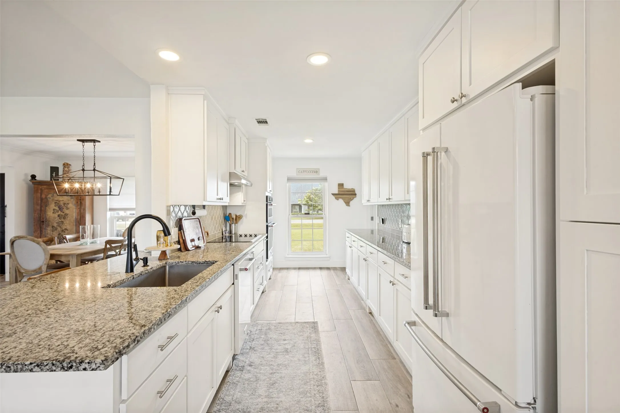 Galley kitchen featuring extensive white cabinetry, light-toned wood-finish flooring, and granite countertops