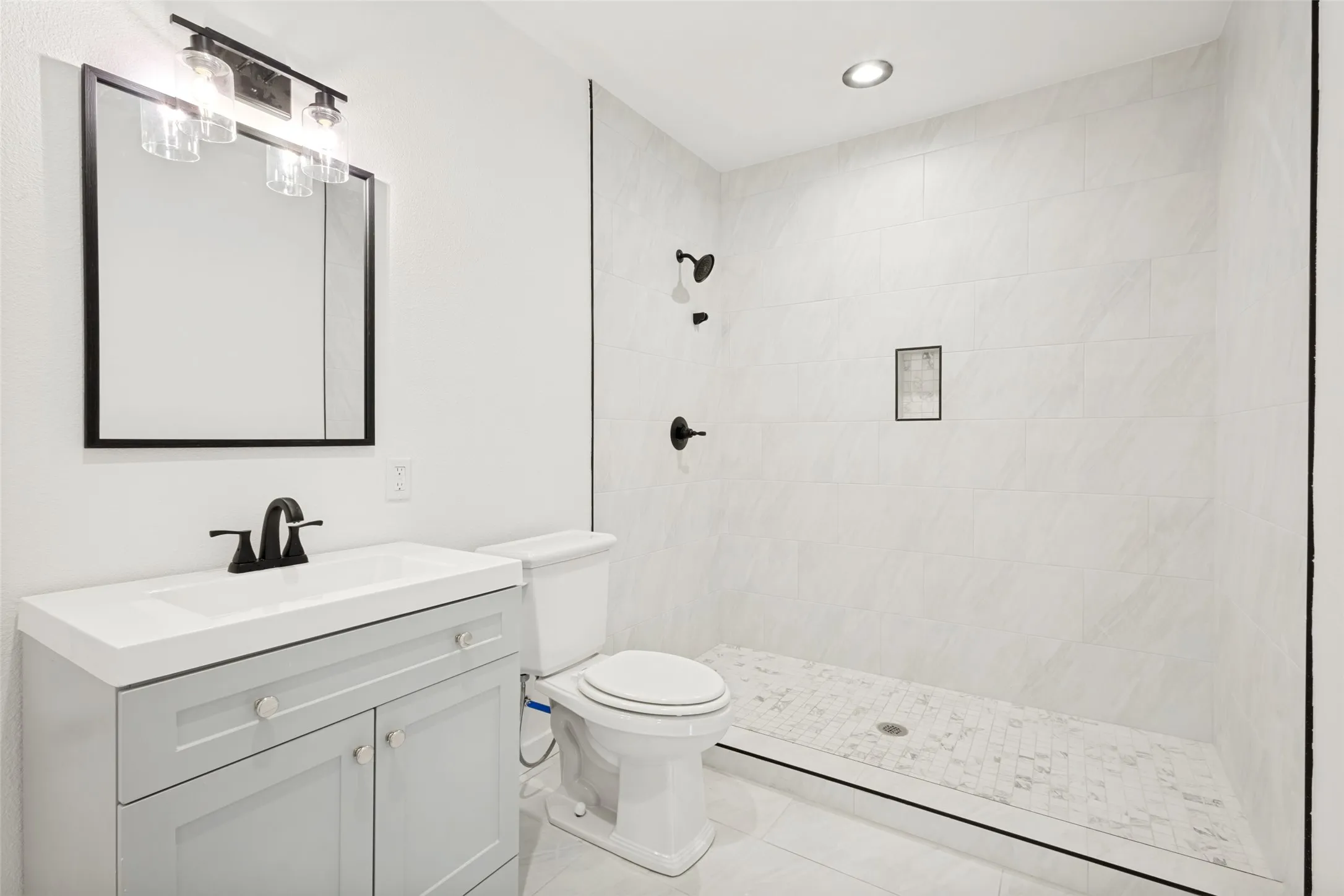 Guest house -Bathroom featuring a light gray vanity with an integrated white sink, a matte black faucet, and a rectangular mirror. Also has washer and dryer connections