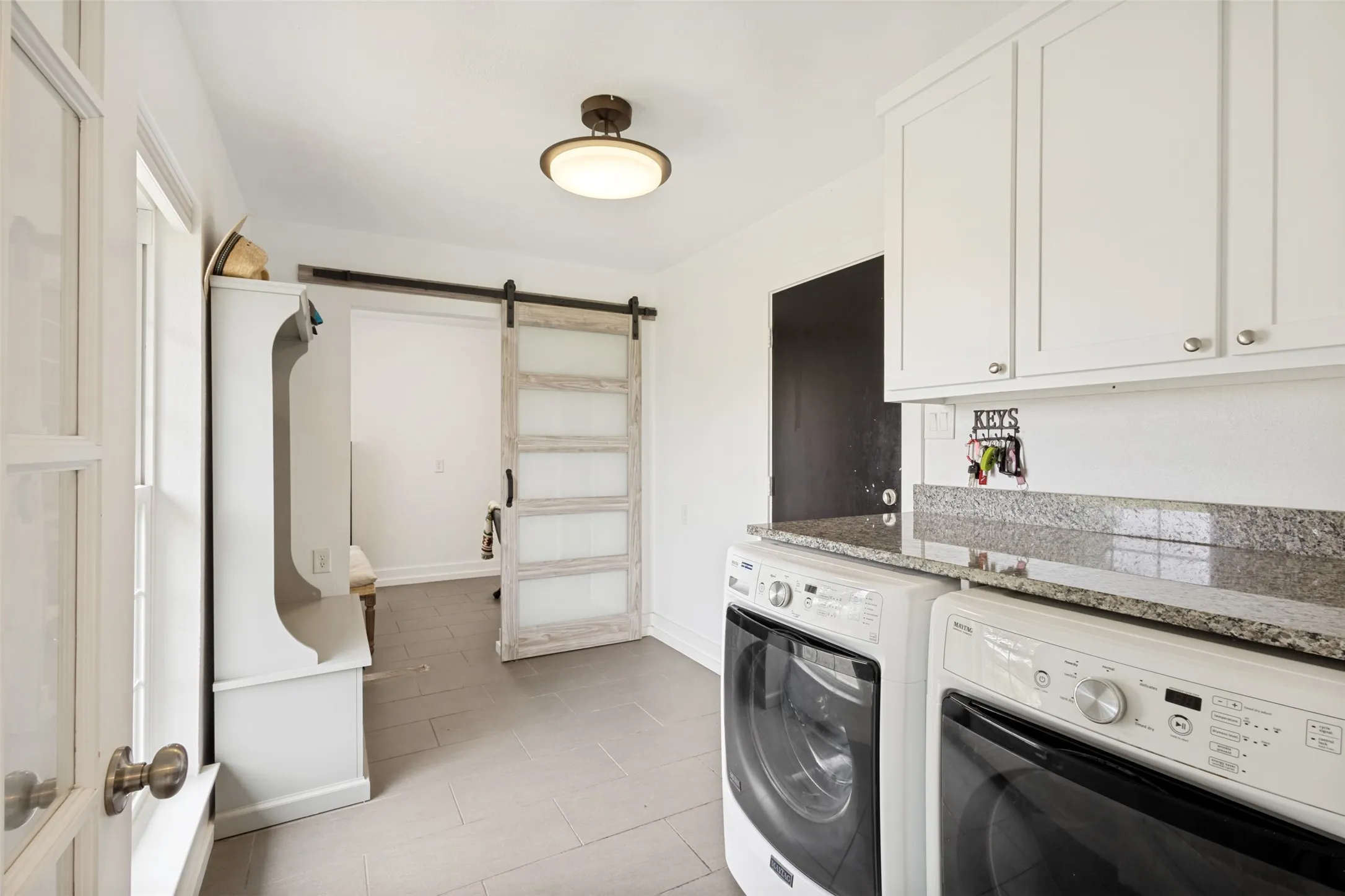 Utility space featuring a barn door entry, white shaker-style cabinetry, a stone countertop, and tile flooring