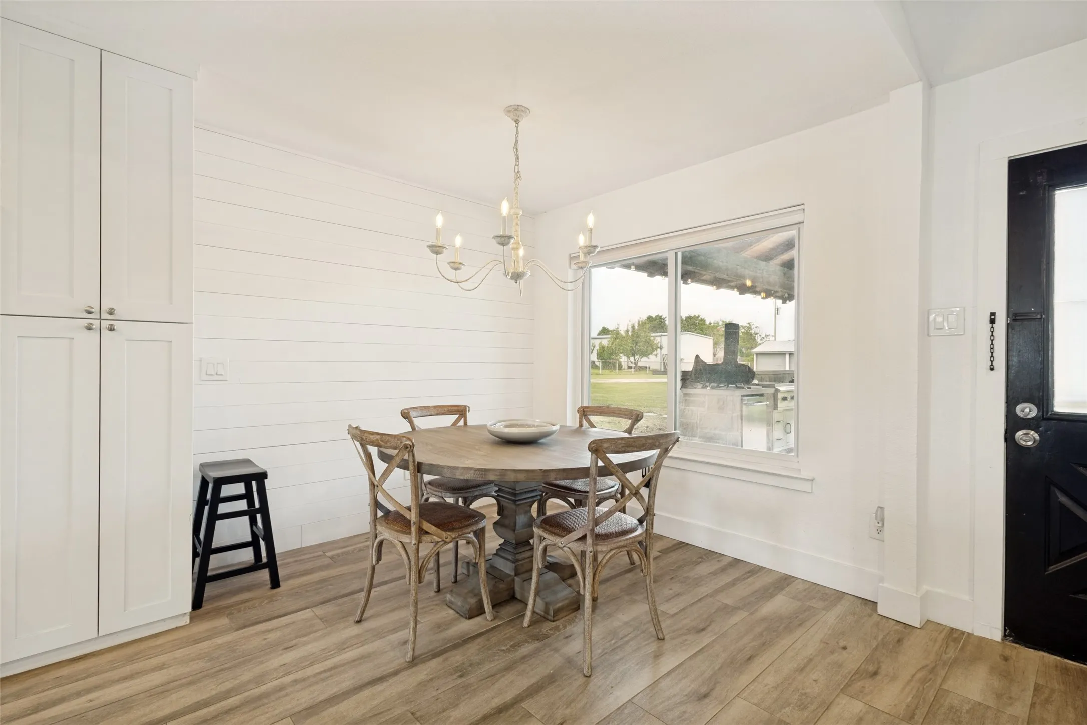 Dining area featuring wood-finish flooring, shiplap accent wall, white baseboards, a large window, and a built-in white storage cabinet