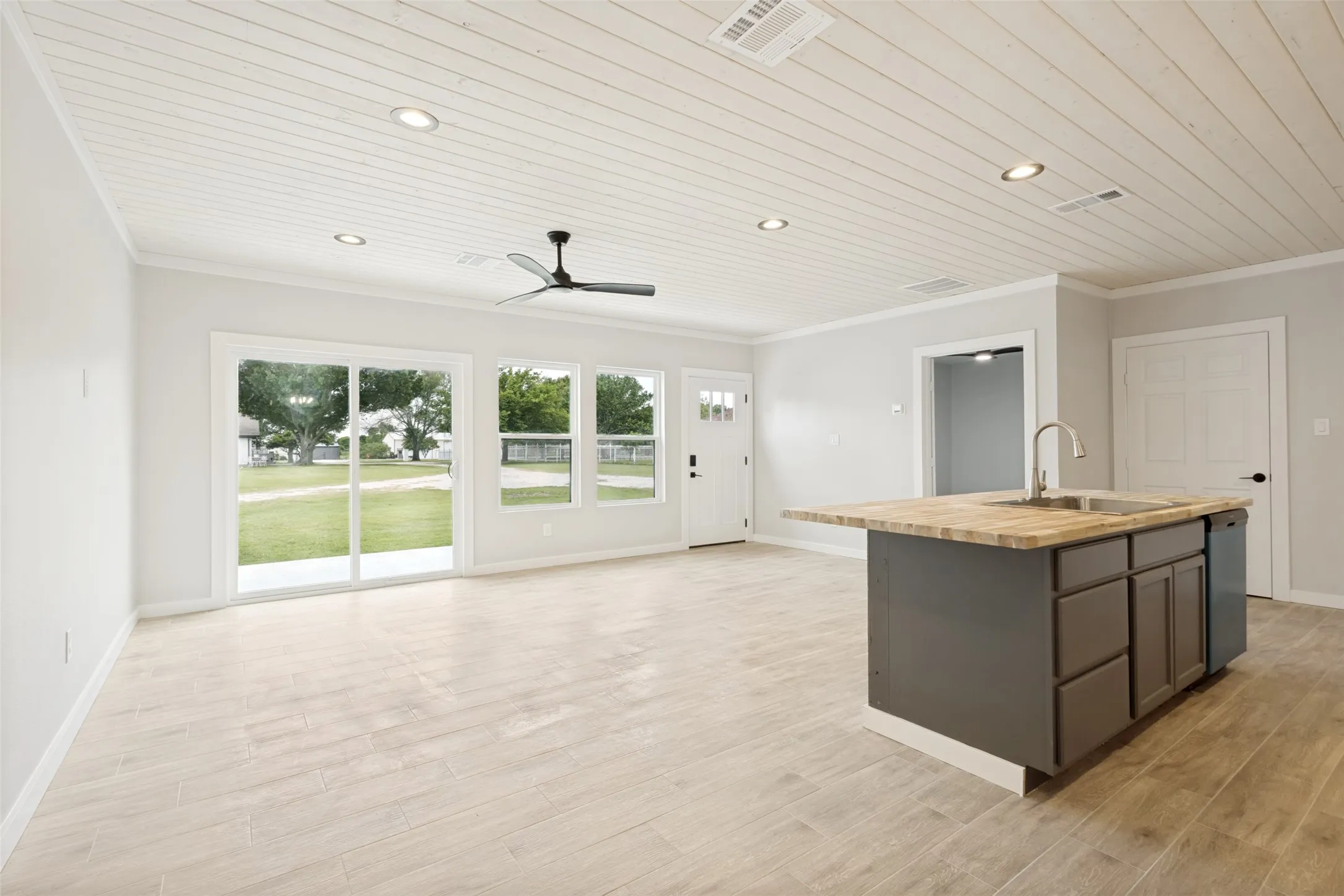 Guest house - Open concept room featuring light wood-finish flooring, white shiplap ceiling with recessed lighting and a ceiling fan, and multiple windows