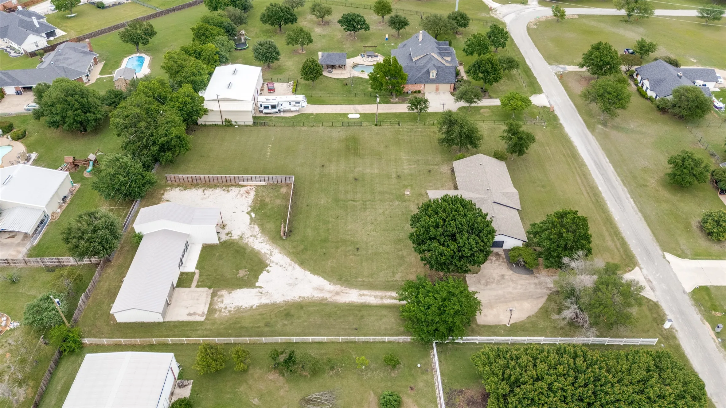 Expansive property featuring a gravel driveway, mature trees, a main residence with a gabled roof, and a secondary structure with a metal roof