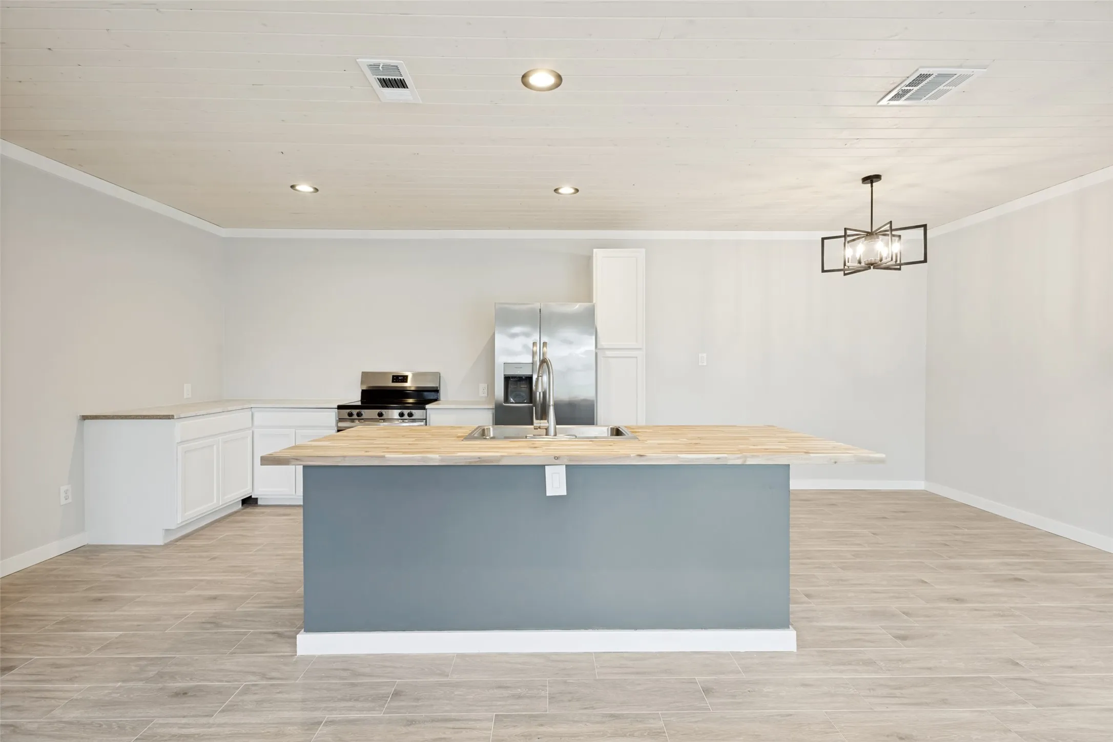 Guest house -Spacious kitchen featuring a central island with a wood-finish countertop, white cabinetry, stainless steel appliances, and wood-finish tile flooring