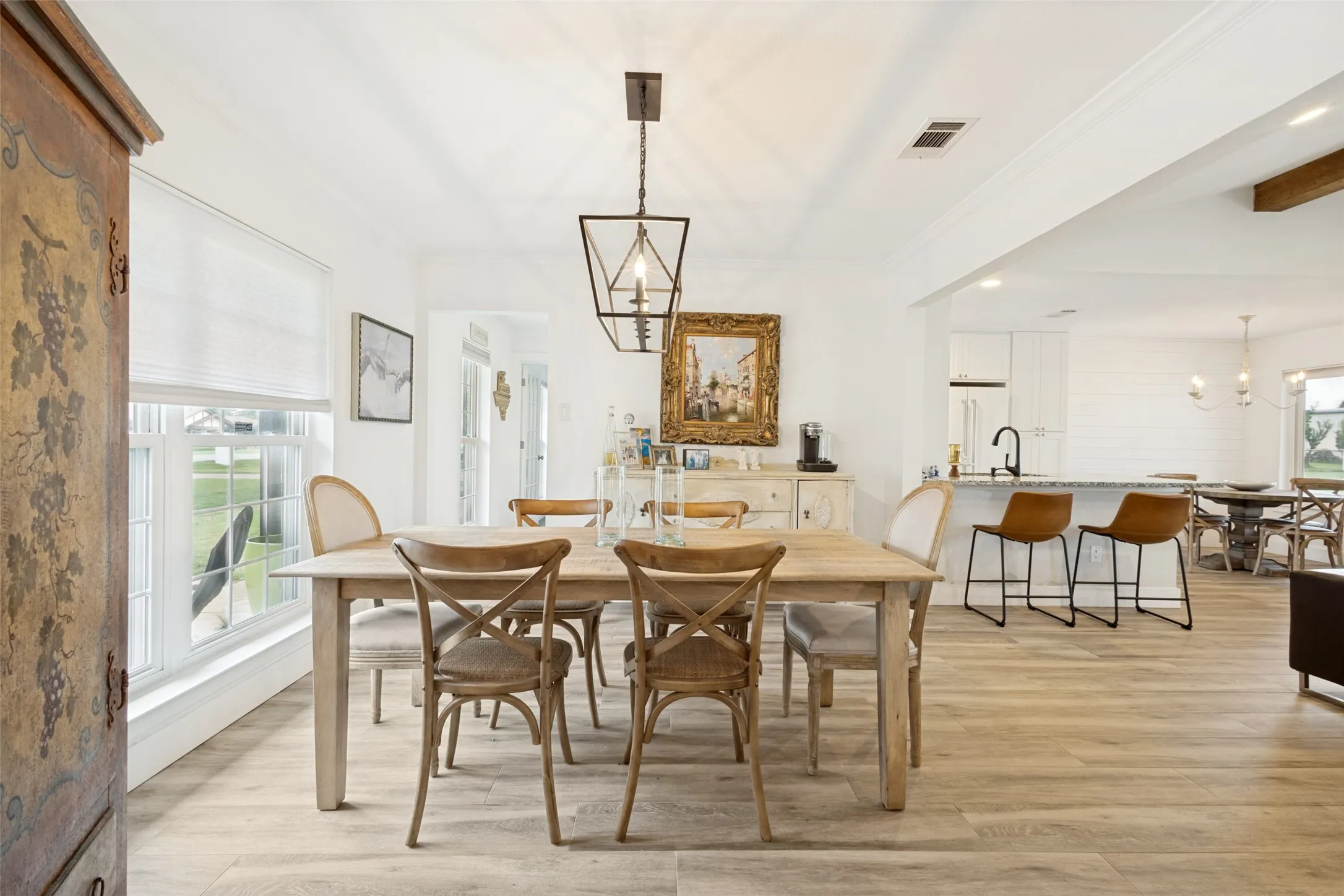 Open-concept dining area featuring wood-finish flooring, a contemporary chandelier, multiple windows, and a clear sightline to the kitchen with an island