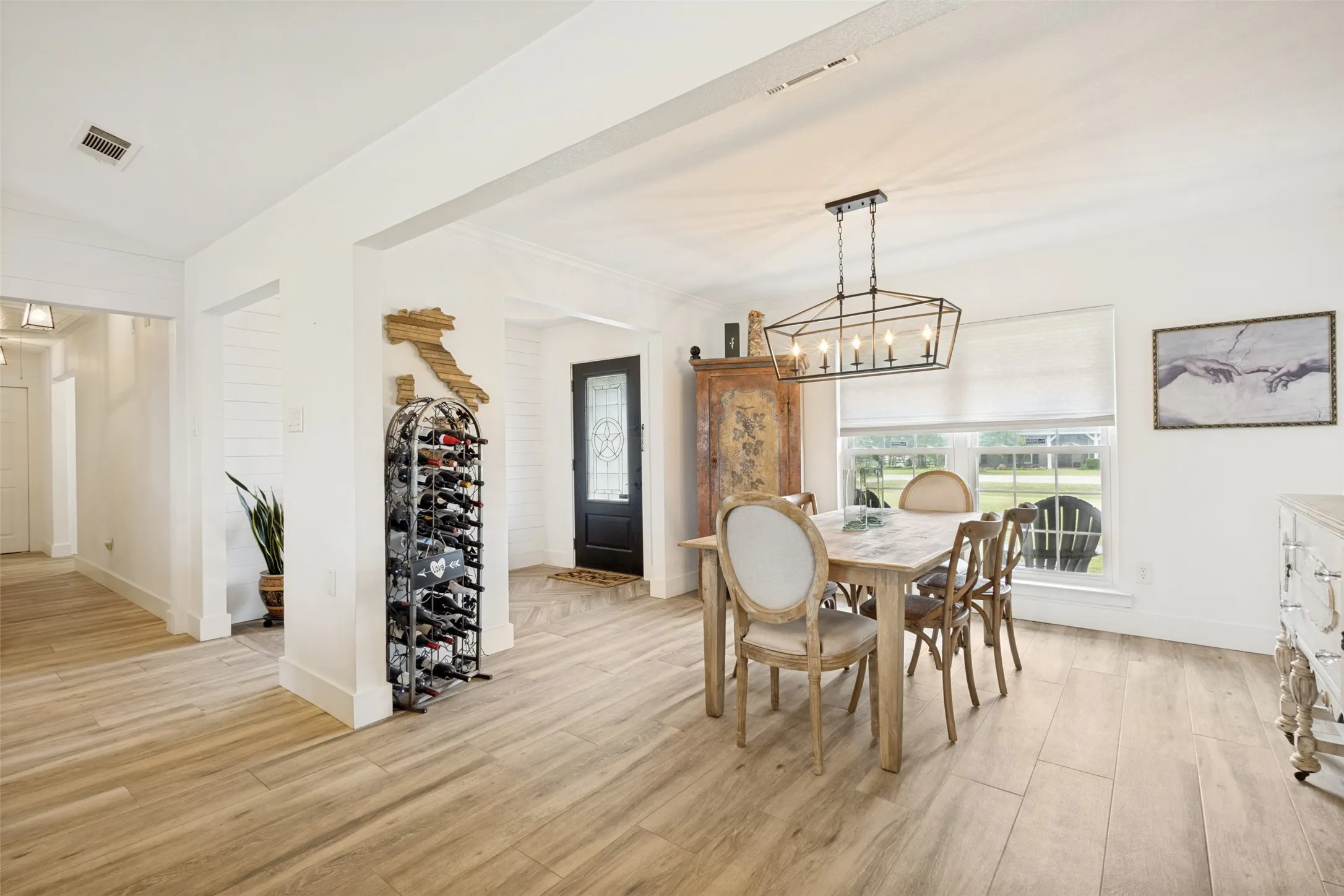 Open-concept room featuring wood-finish flooring, white walls, and a contemporary chandelier