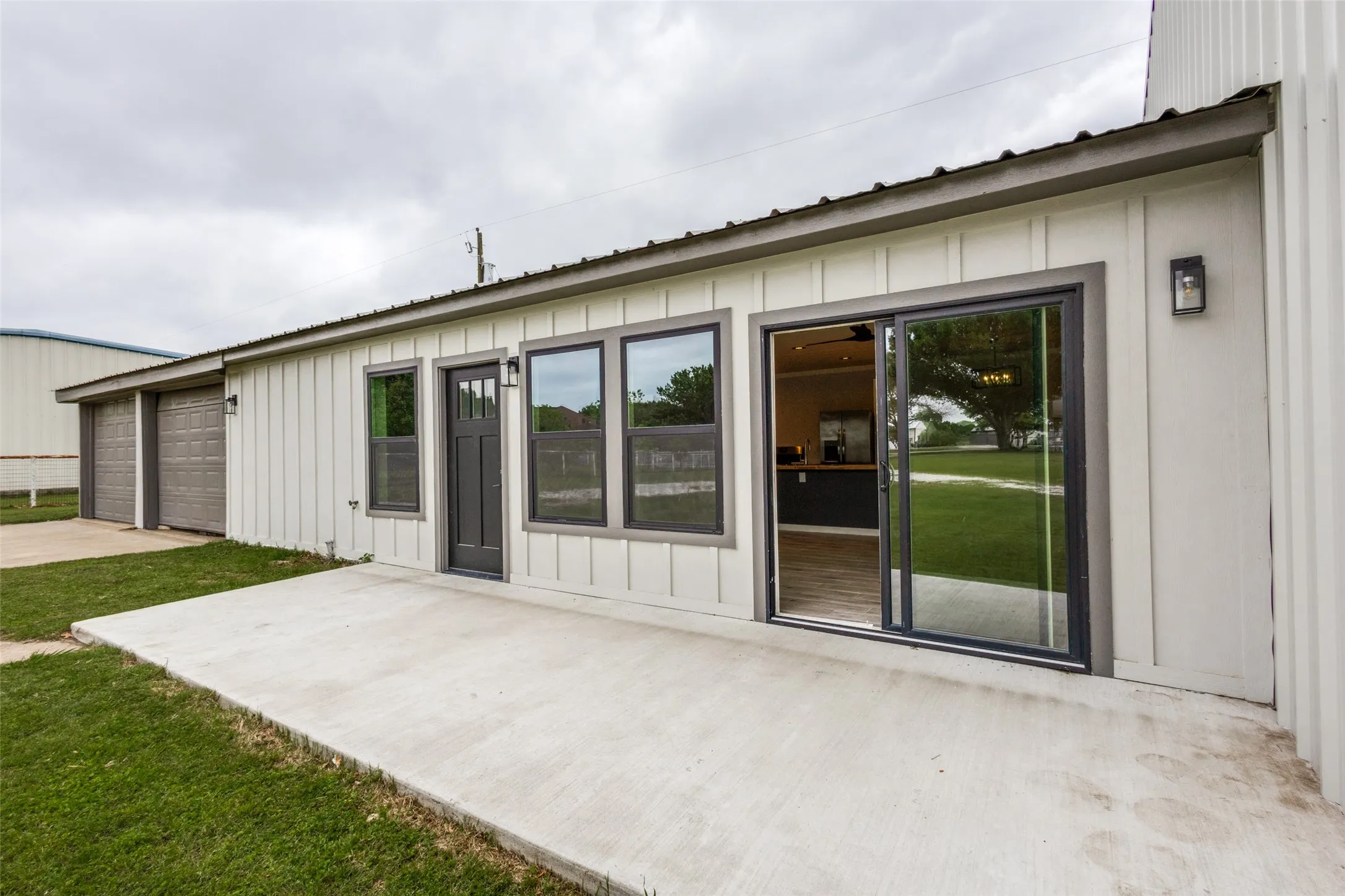Guest house - Exterior patio featuring a concrete slab, board and batten siding, dark framed windows, a dark framed glass sliding door, and a dark entry door