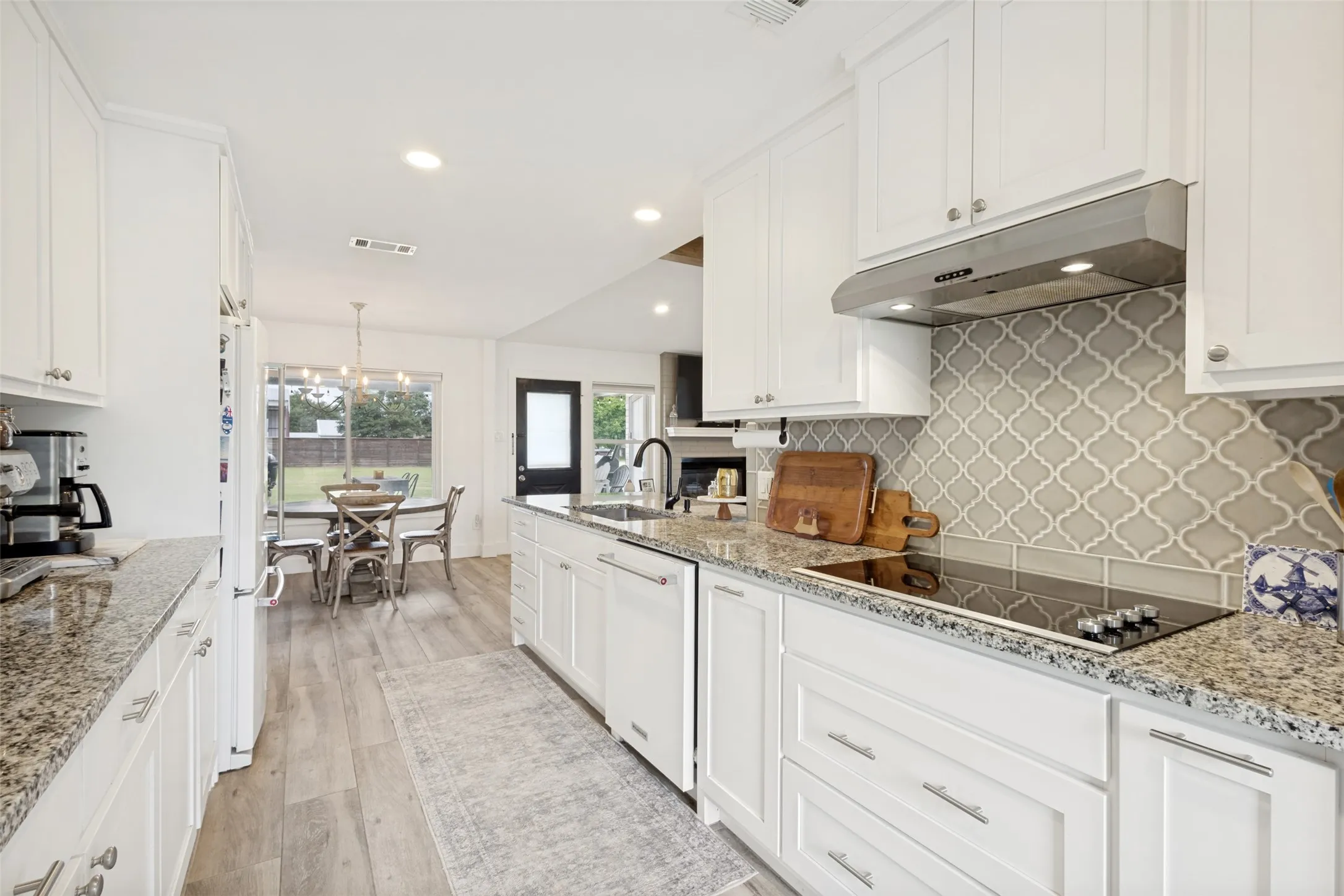Kitchen featuring white cabinetry, granite countertops, an integrated cooktop, a tile backsplash with an arabesque pattern, and wood-finish flooring