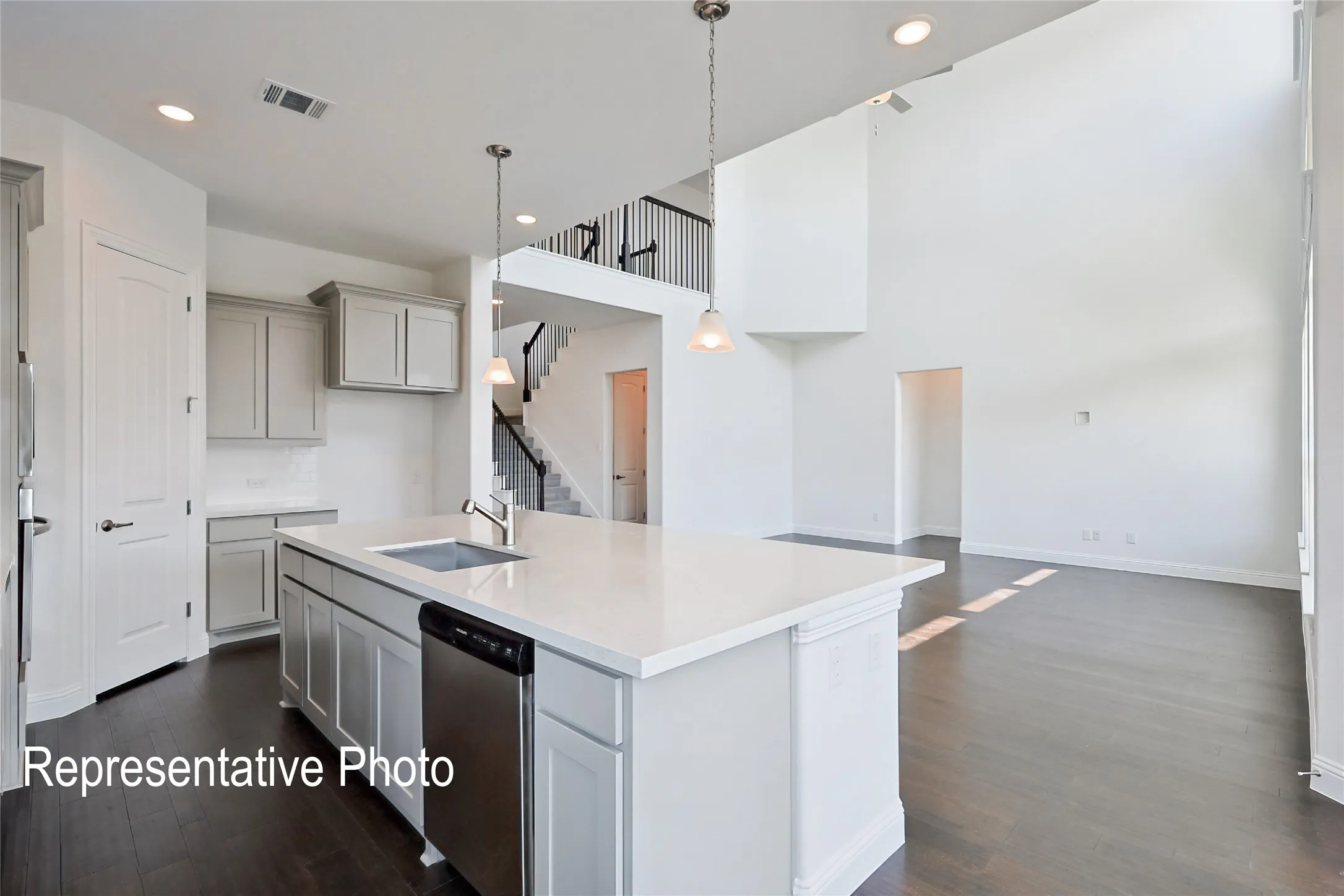 Open-concept living space featuring high ceilings, dark wood-finish flooring, and a kitchen island with a built-in sink and stainless steel dishwasher