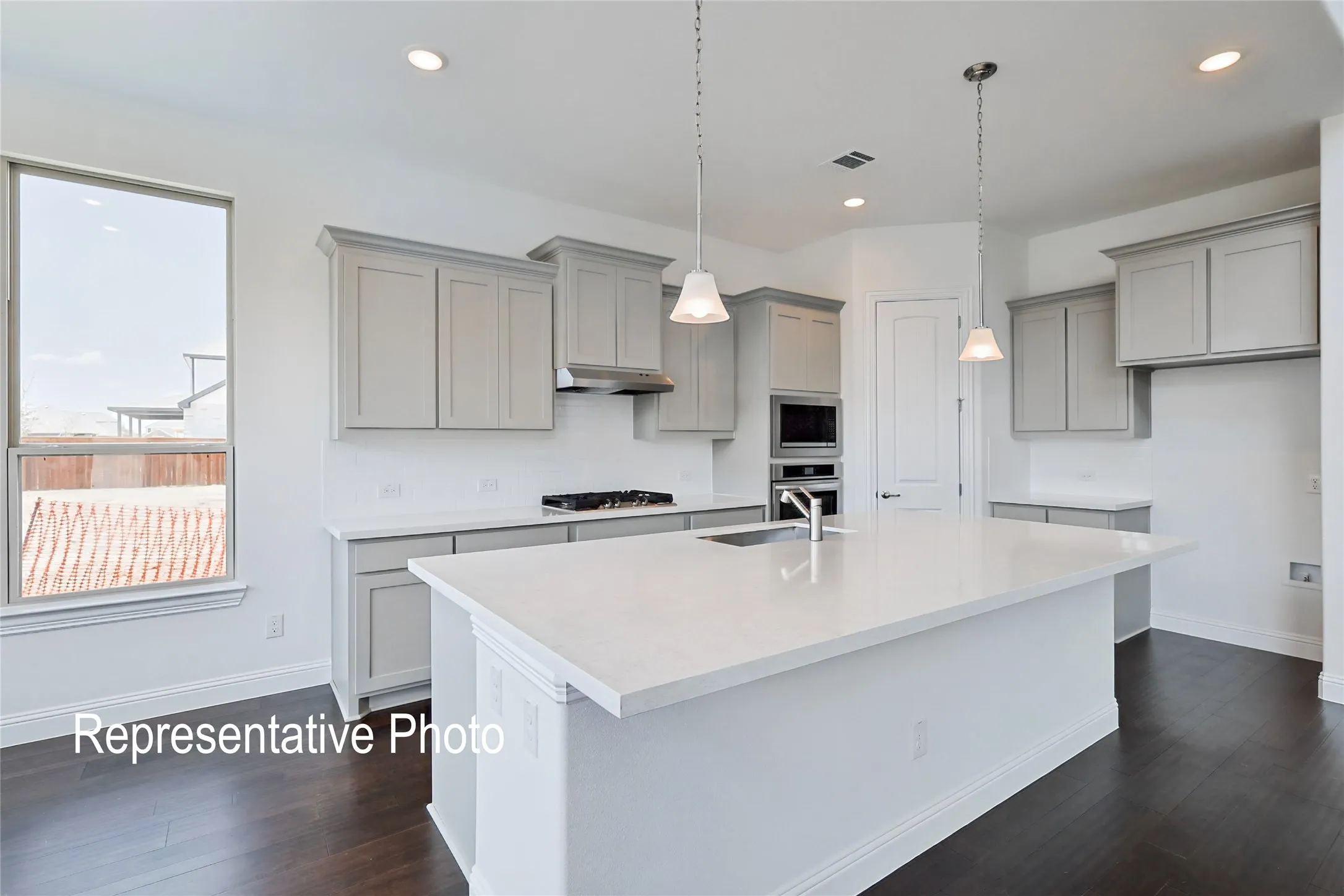 Modern kitchen featuring light gray cabinetry with crown molding, a large central island with a white solid surface countertop, and stainless steel built-in appliances