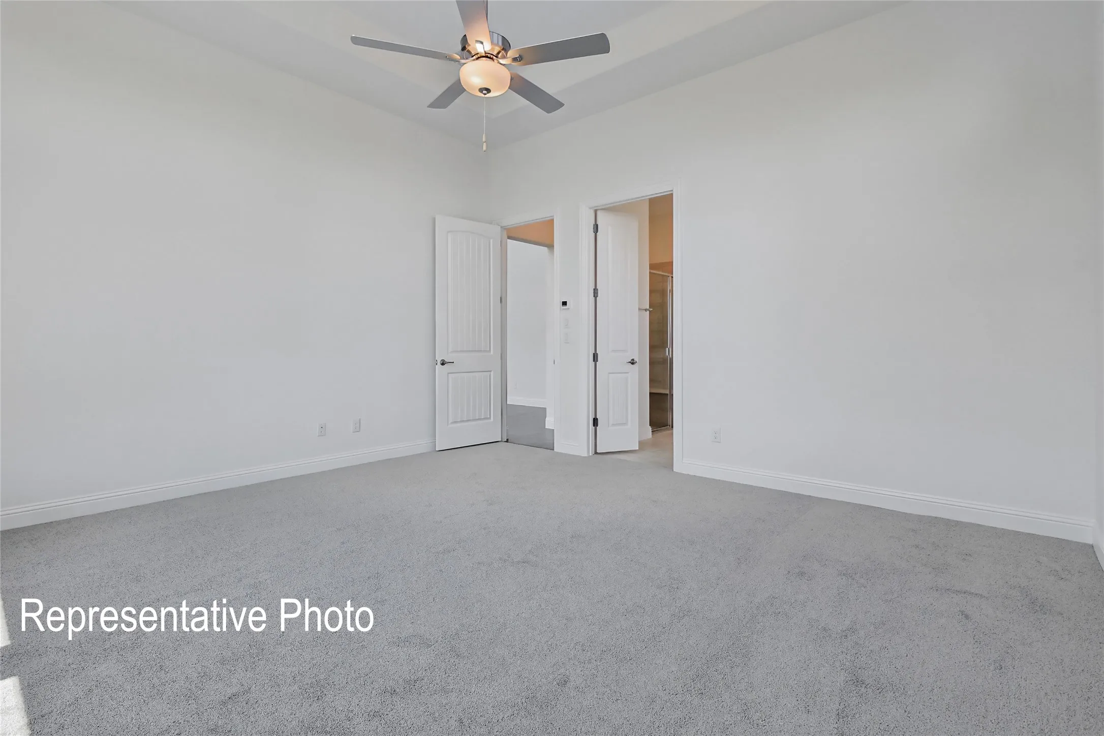 Spacious room featuring light gray carpeting, crisp white walls, a tray ceiling, and a ceiling fan with integrated lighting