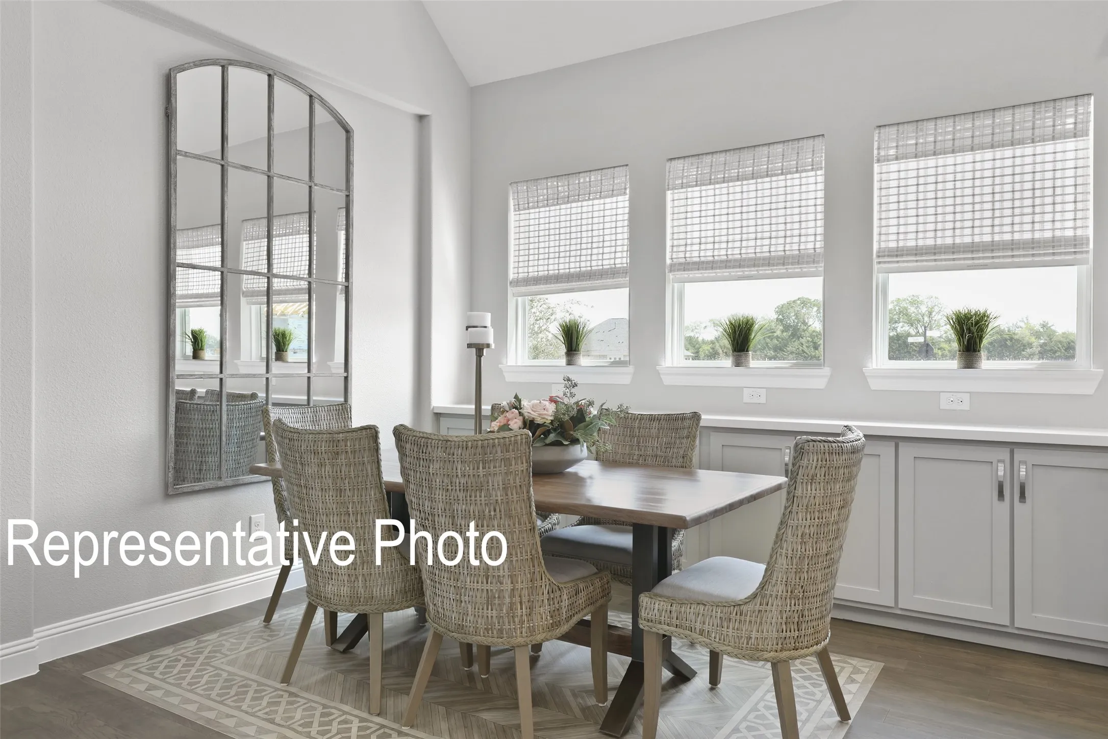 Dining area featuring vaulted ceilings, light gray wall color, three windows with natural light, built-in lower cabinetry with a light-colored countertop, and wood-finish flooring