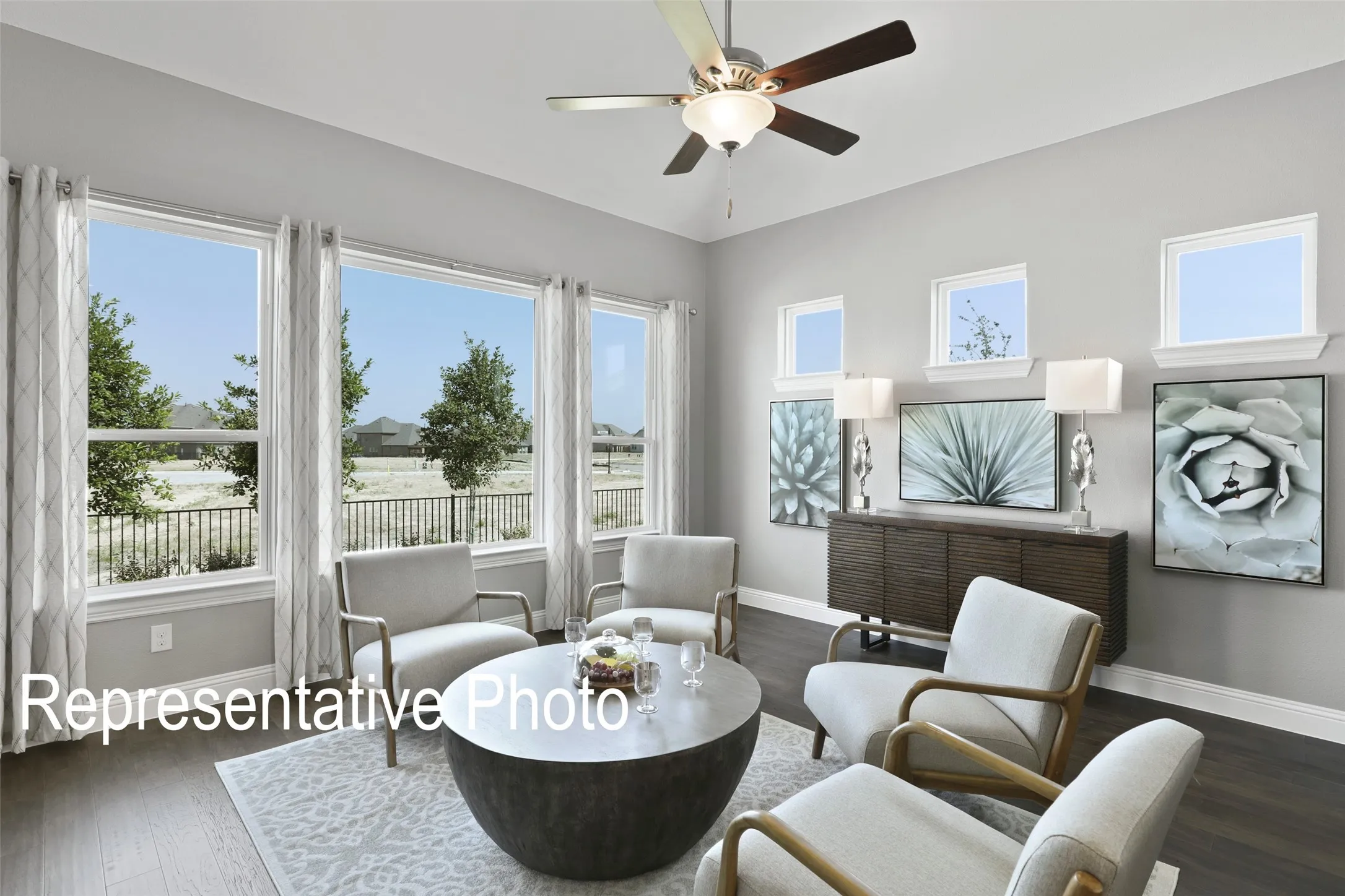 Spacious living area featuring expansive windows, wood-finish flooring, a ceiling fan with integrated lighting, and a built-in credenza