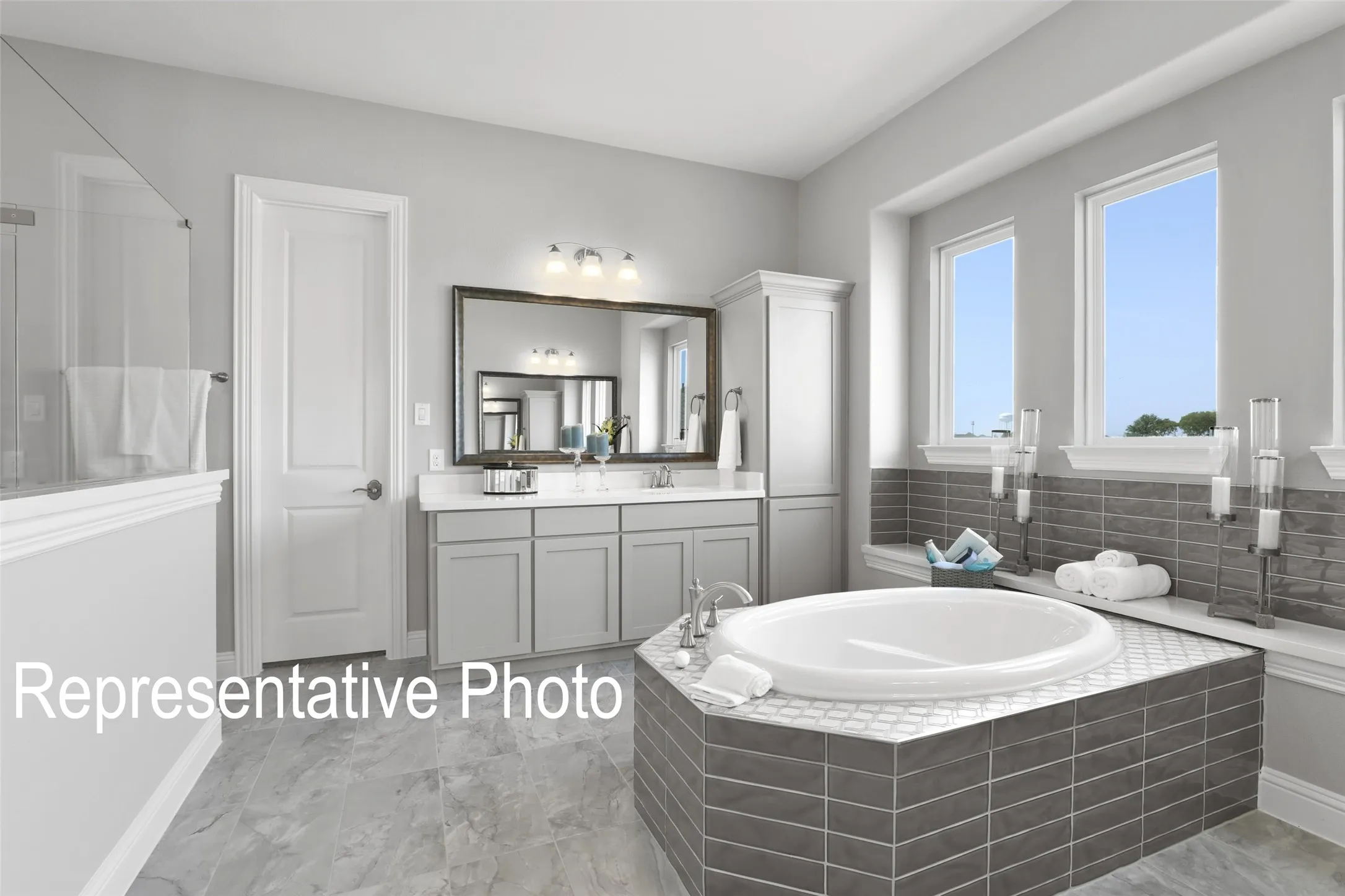 Bathroom featuring a built-in soaking tub with gray subway tile surround, double vanity with gray cabinetry and white countertops, large wall-mounted mirror, and a separate glass-enclosed shower