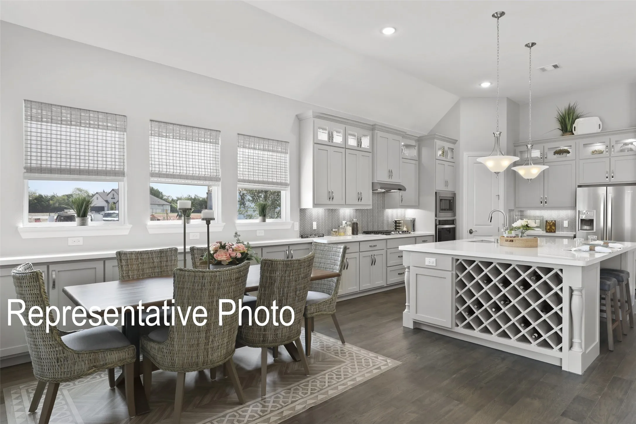 Spacious open-concept kitchen featuring light-toned cabinetry, stainless steel appliances, a central island with integrated wine storage, and wood-finish flooring