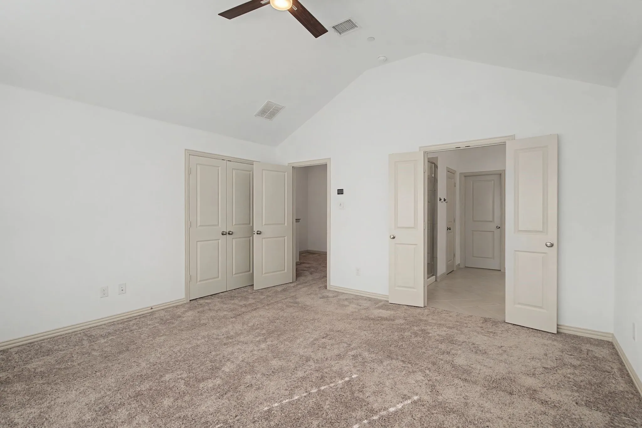 Spacious room featuring vaulted ceilings, light neutral carpeting, and a ceiling fan